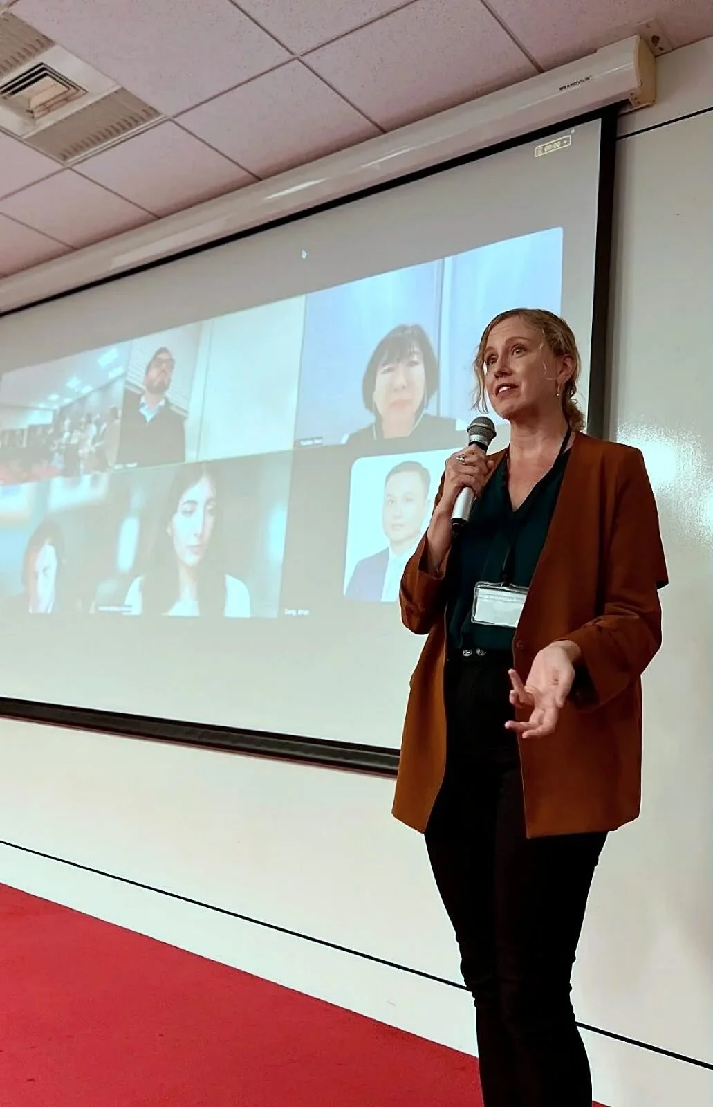 Heather Dobbin delivering a keynote speech at a hybrid international conference in Tokyo, engaging both in-person and virtual audiences