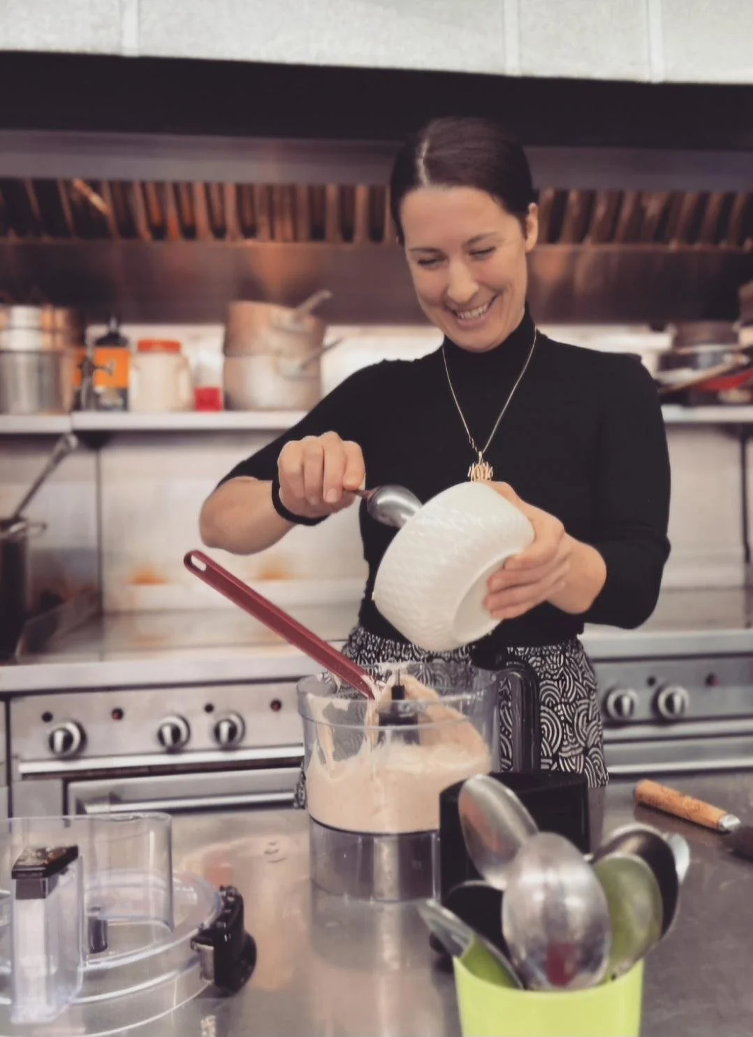 A woman smiling in a kitchen, scooping ice cream into a container.