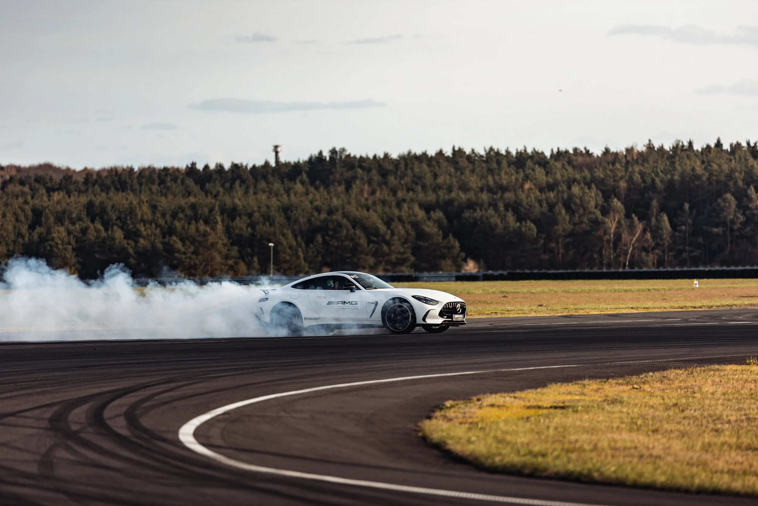 Biały sportowy Mercedes-AMG w trakcie driftu na torze wyścigowym – efektowny dym spod kół.