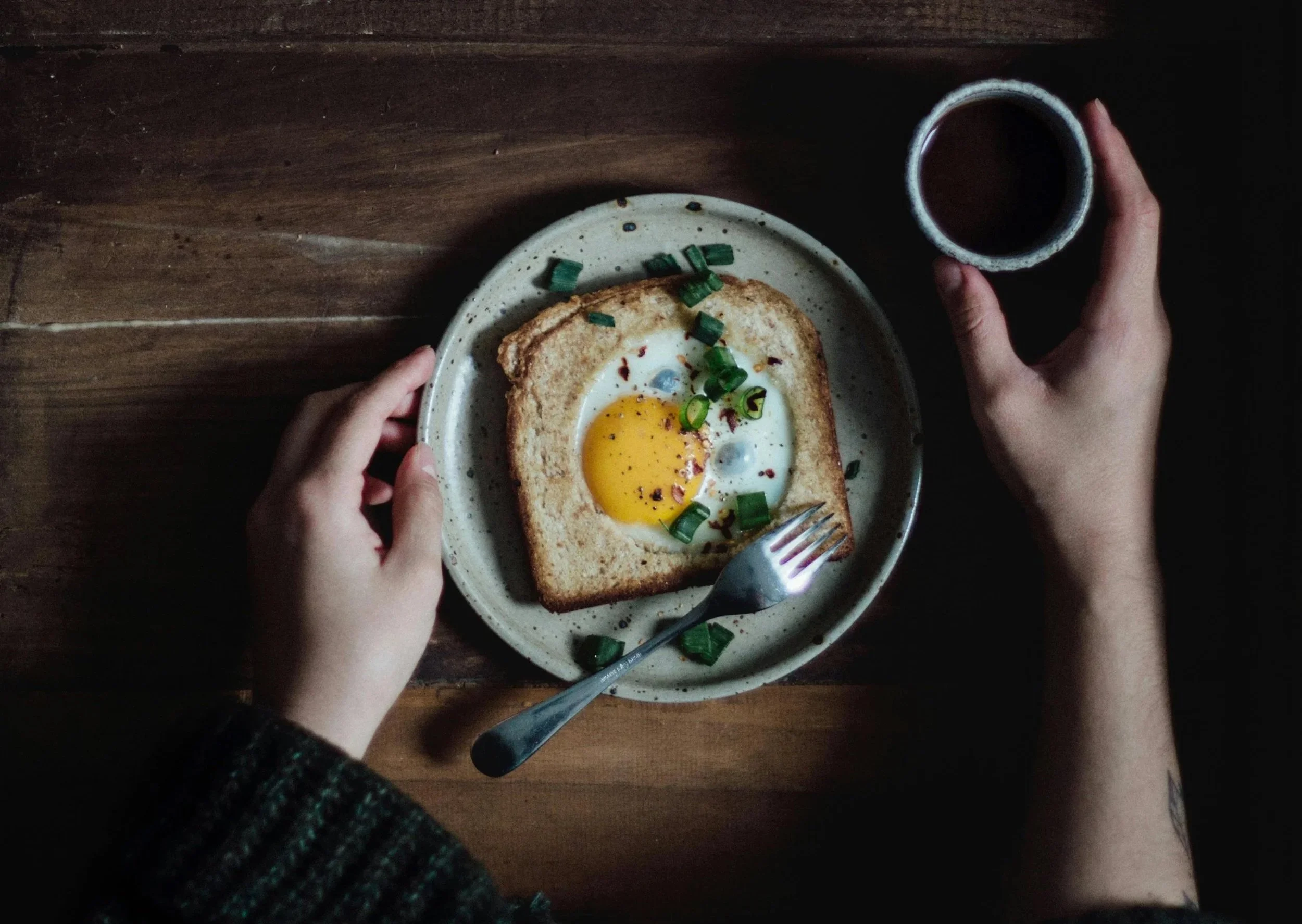 A woman’s hands holding egg-in-toast with a cup of coffee, reflecting a slow and intentional summer morning