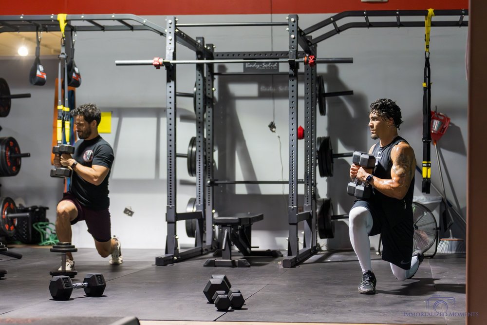 Two athletes doing dumbbell lunges in a coached class