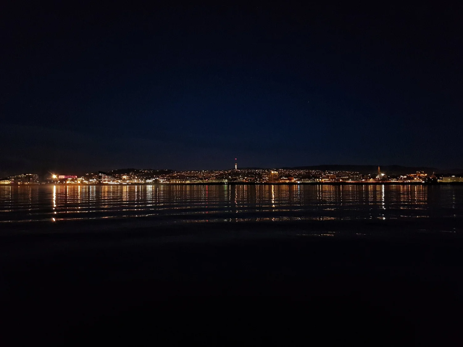 Trondheim city lights reflected across the fjord during an evening boat trip