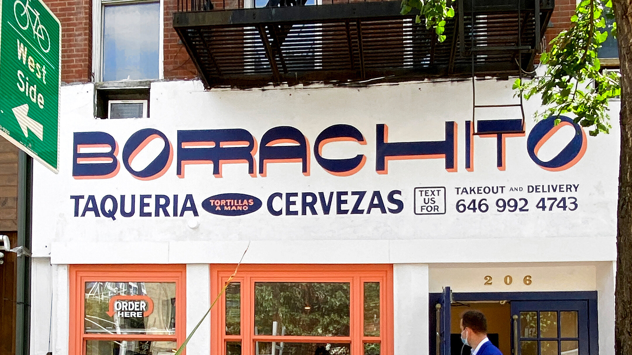  White storefront with “Borrachito” handpainted on the facade in dark blue with an orange drop shadow, in a funky decorative lettering style 