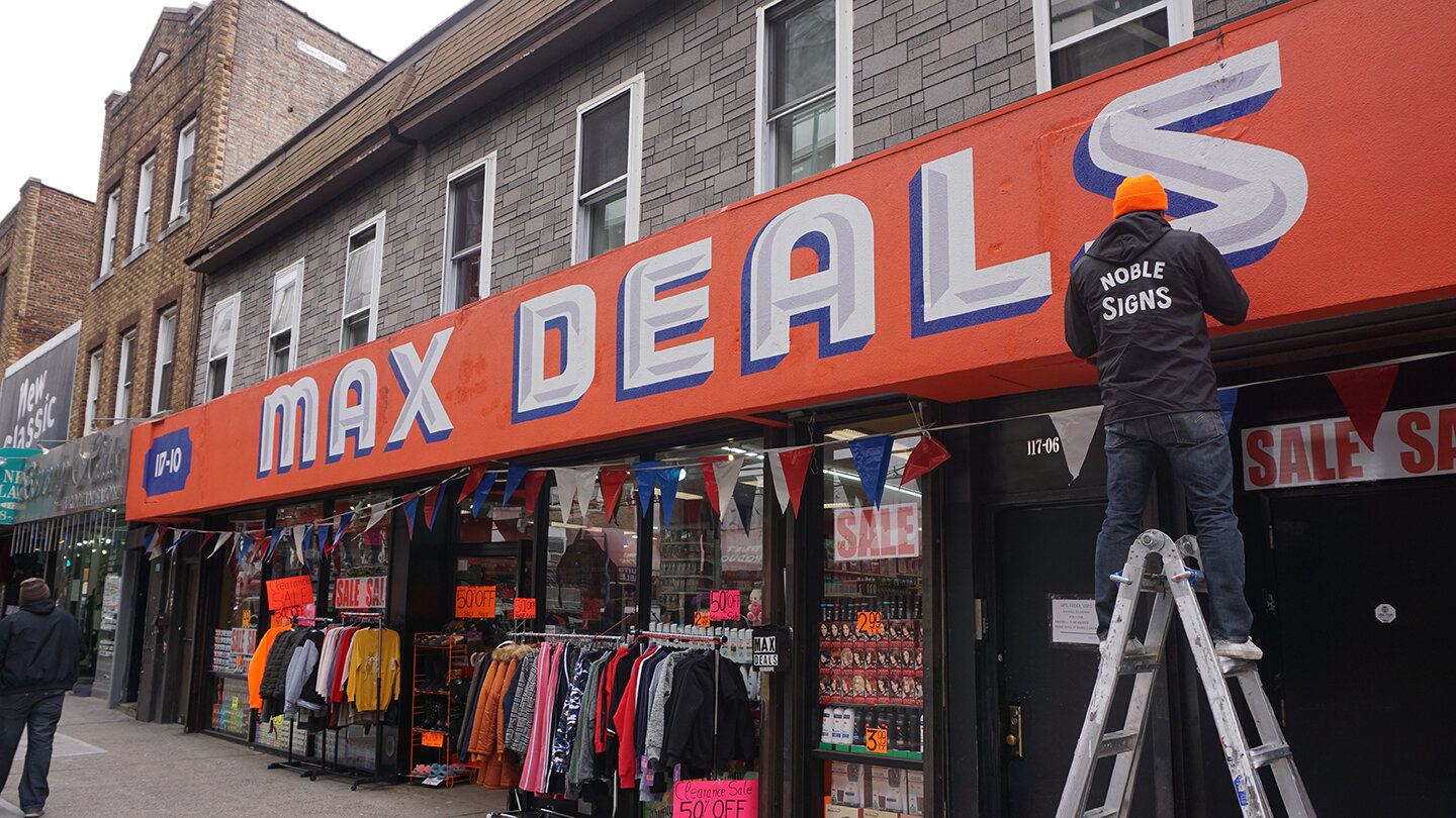  Large storefront sign reading “Max Deals” in white with a blue drop shadow on a red backdrop 