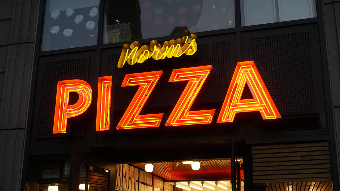  Storefront sign reading “Norm’s Pizza” in script and block letters, fabricated using custom channels and yellow and red concentric neon tubing 