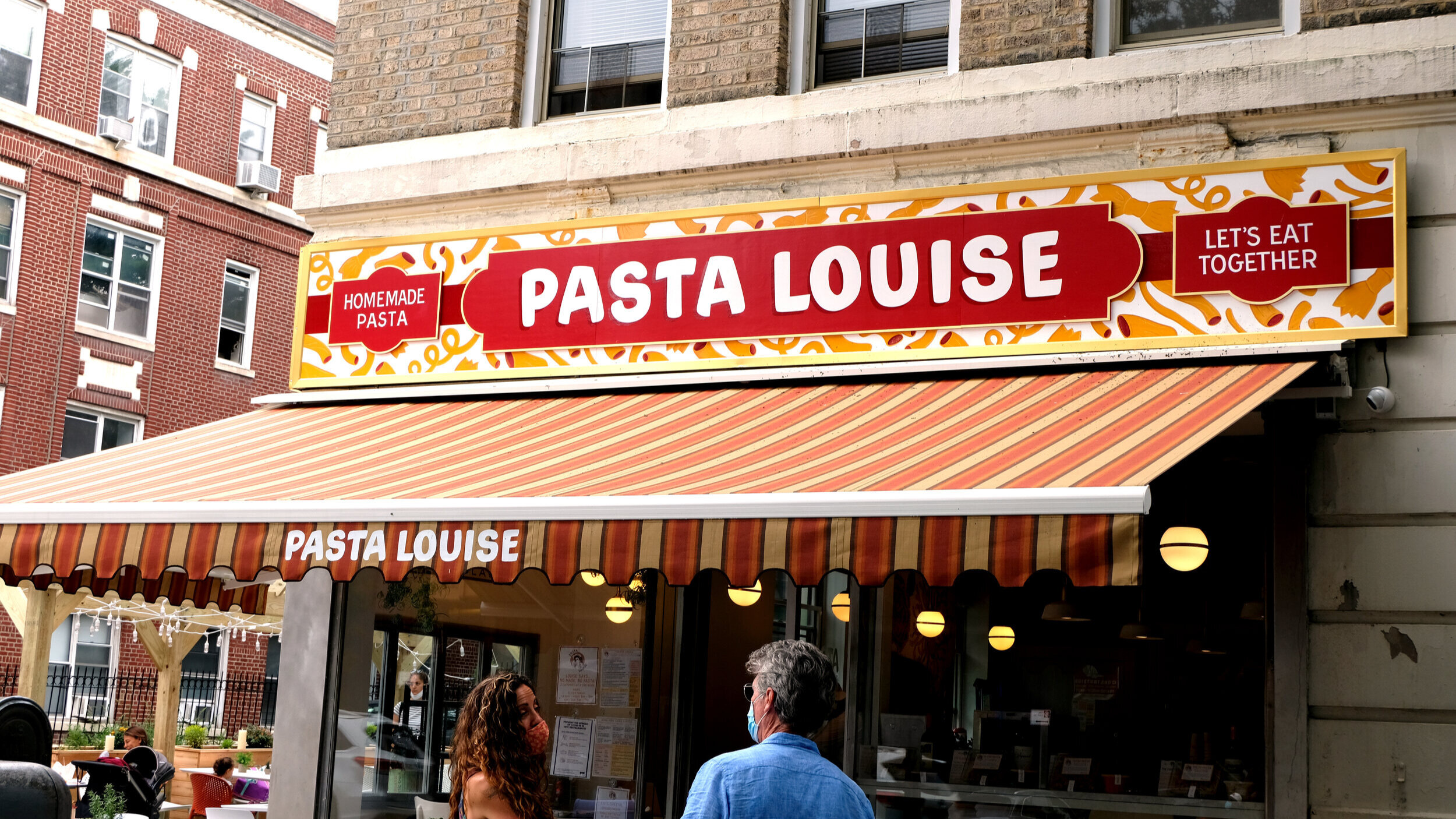  Storefront sign reading “Pasta Louise” in white handpainted casual lettering in a red frame, surrounded by yellow pasta shapes on a white background 