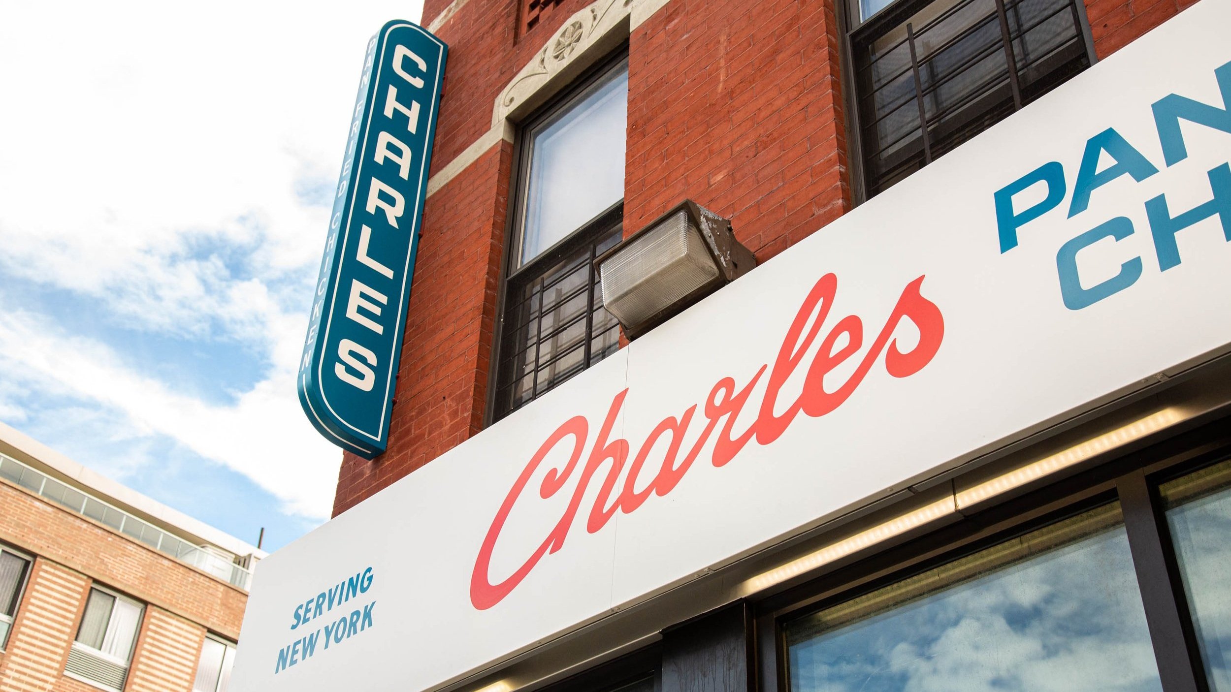  Close-up of topsign reading “Charles Pan-Fried Chicken” in handpainted red script lettering and blue block lettering on white backdrop and a blue vertical blade sign with white lettering reading “Charles” 