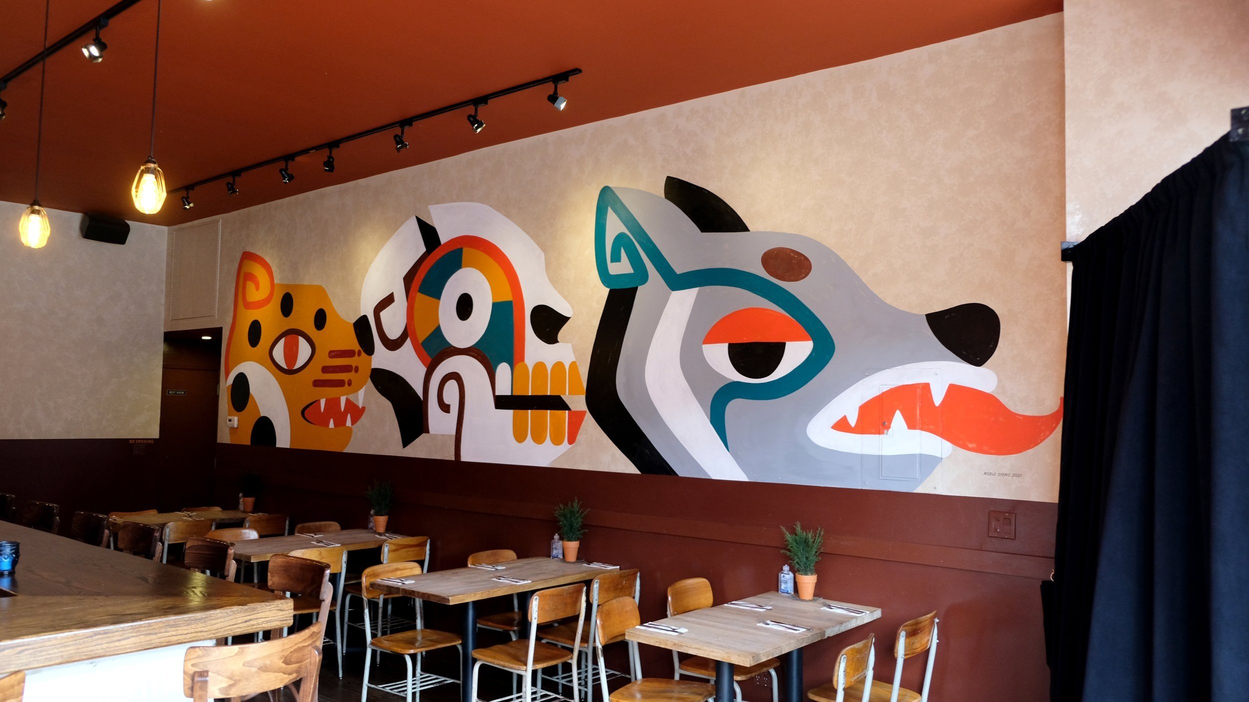  A handpainted interior mural of a jaguar, a skull, and a wild dog emulating ancient Aztec calendar art in yellow, white, gray, teal, black, and orange paint 
