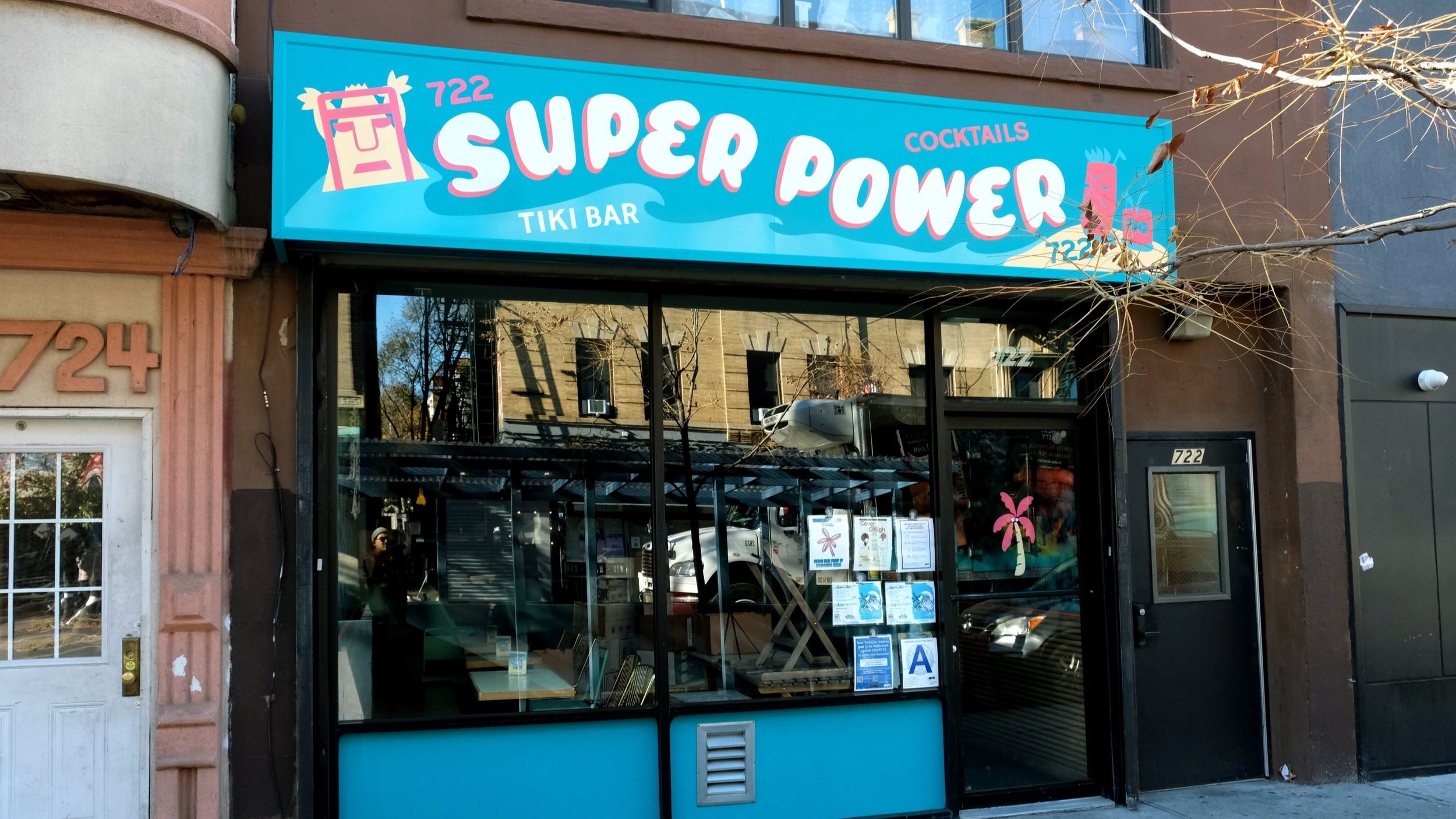  Light blue storefront sign reading “Superpower” in white bubbly handpainted letters, surrounded by handpainted tiki bar imagery 