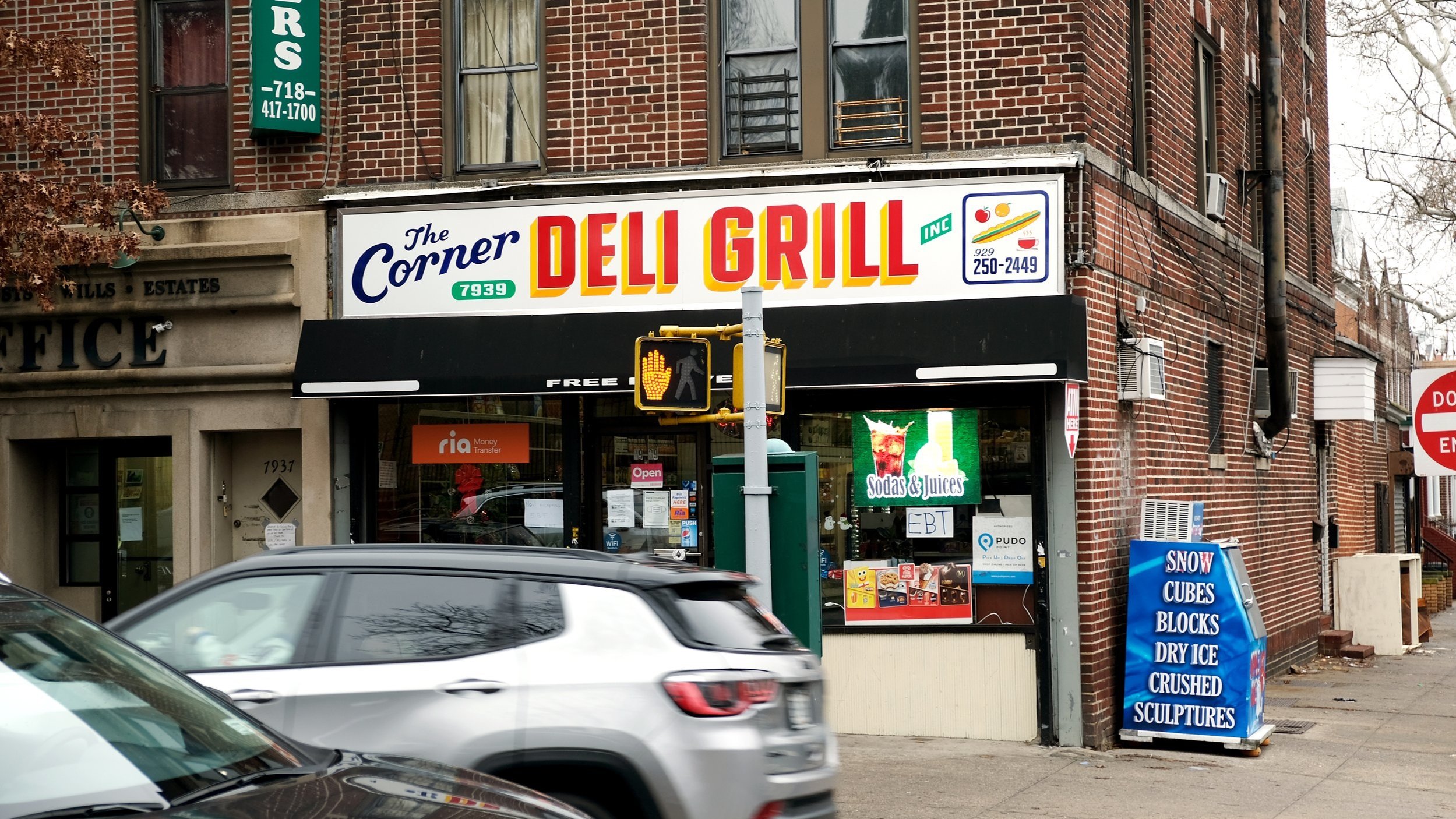  Handpainted corner storefront sign reading “The Corner Deli &amp; Grill” in blue casual script and red with yellow drop-shadow block lettering, as well a small painting of food items 