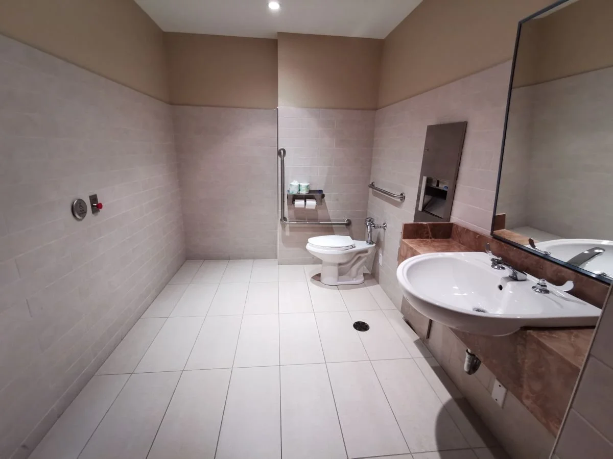 A photo of a bathroom featuring a roll-under sink, grab bars around the toilet, and automated door buttons.