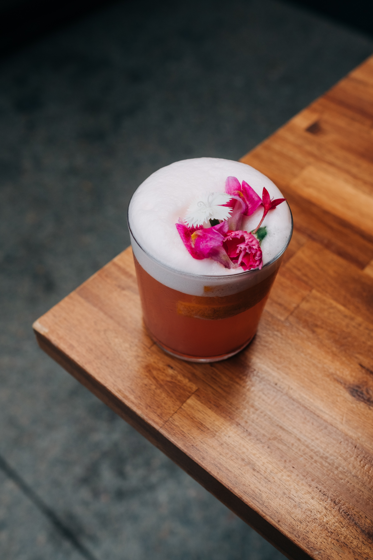 A glass of frothy beverage with pink and white flower garnish on a wooden table.