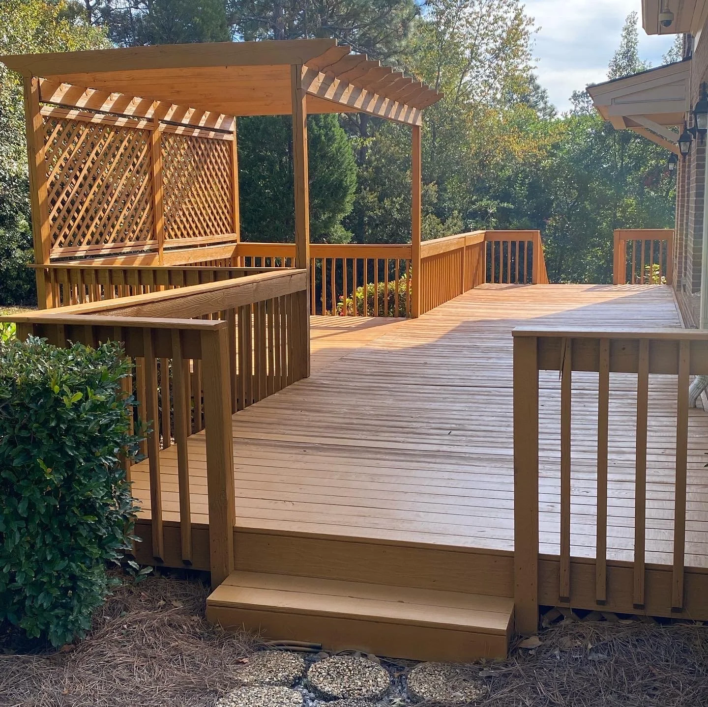 Newly built wooden deck with stairs and a pergola, surrounded by greenery and part of a house.