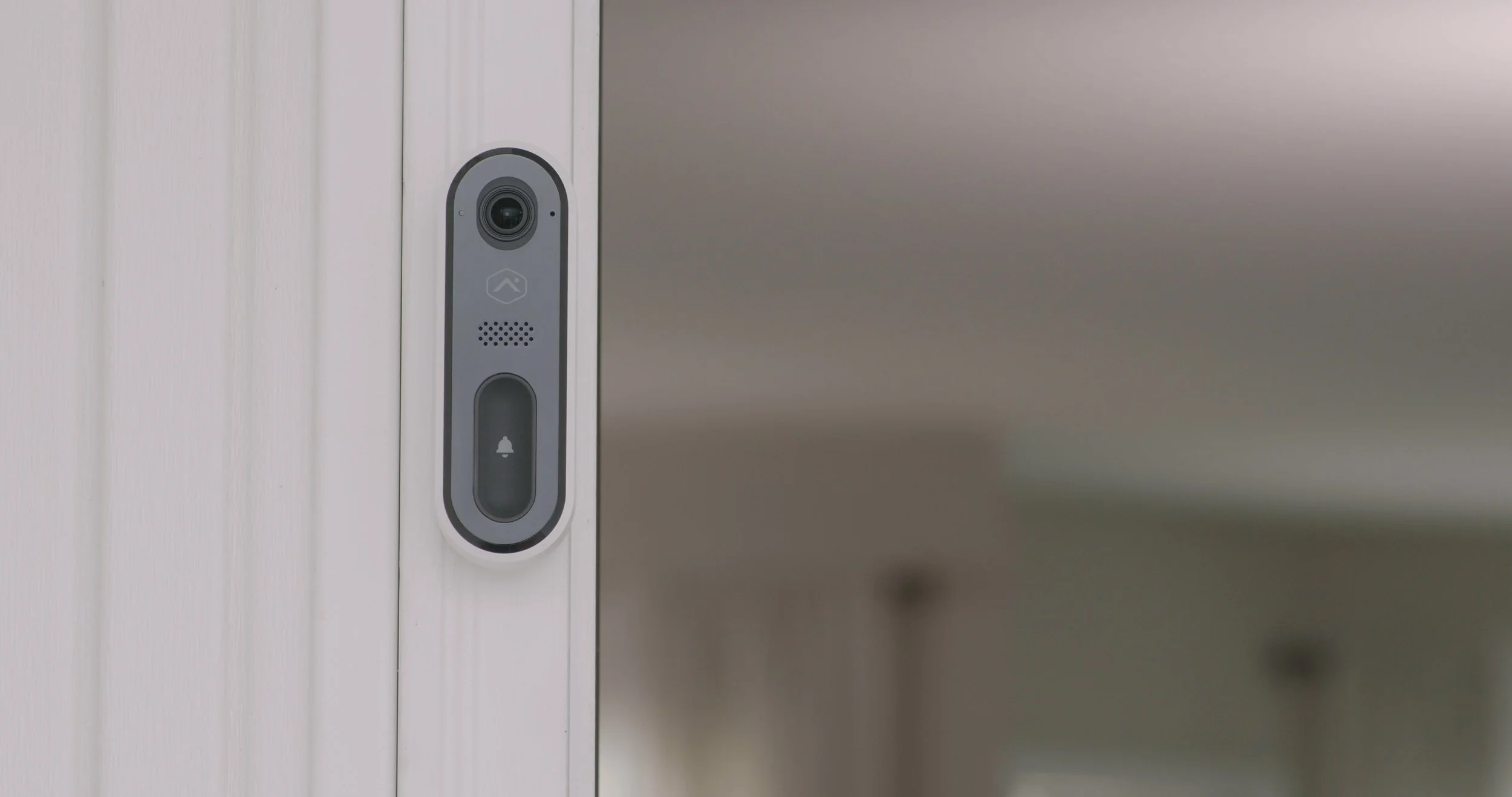 Close-up of a smart doorbell camera mounted next to a doorframe, with a blank wall in the background.
