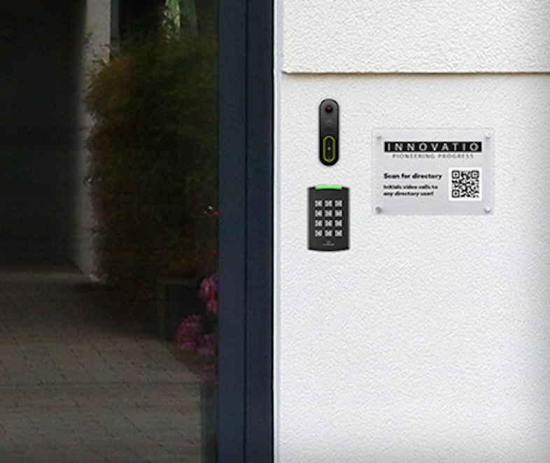 Intercom system and keypad on a white exterior wall near a glass door, with a sign providing instructions and a QR code for digital access.