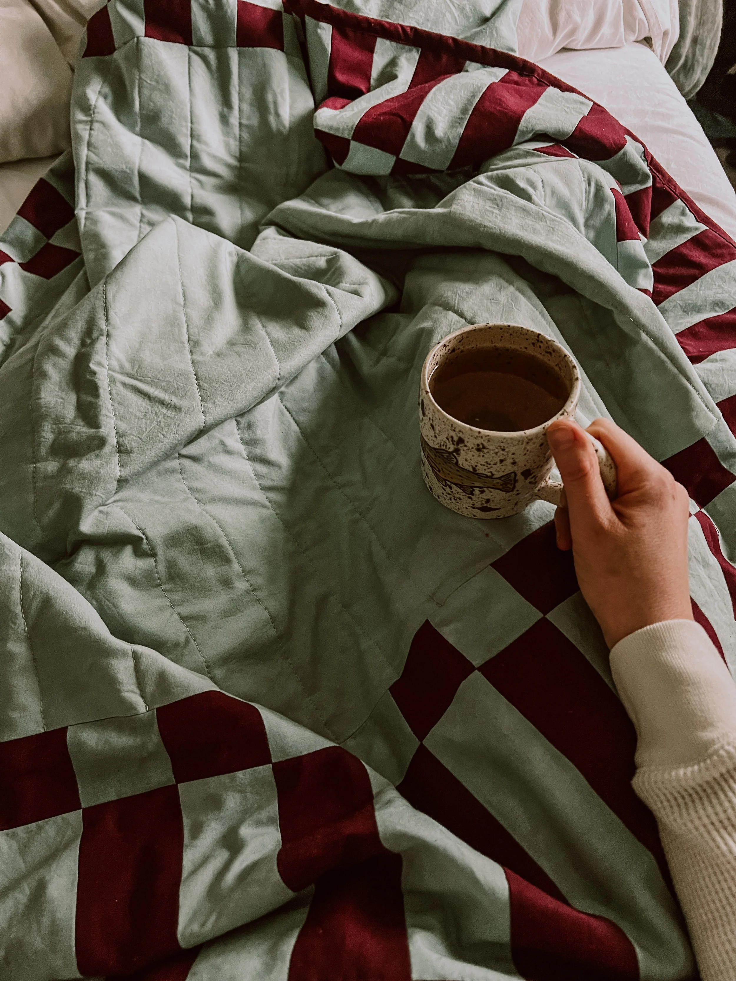 Sage and maroon quilt in bed with cup of tea