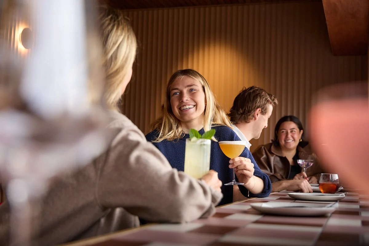 TheKyn-girl holding cocktail at bar smiling with group of people.jpg