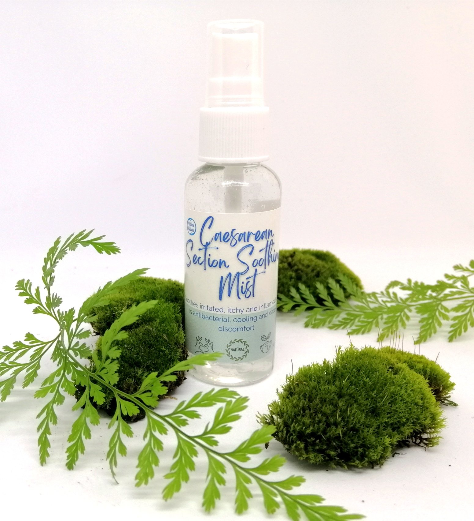 A spray bottle labelled 'Caesarean Section Soothing Mist' surrounded by green moss and fern leaves on a white background.