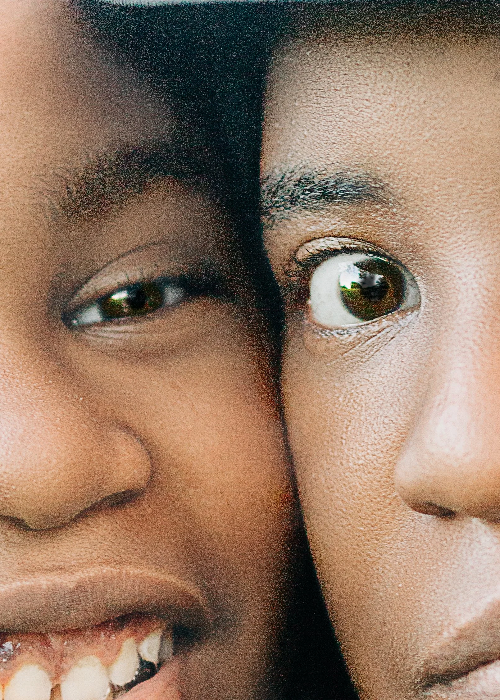 Close-up of two children, one smiling with teeth, both with dark skin and dark hair, facing the camera.