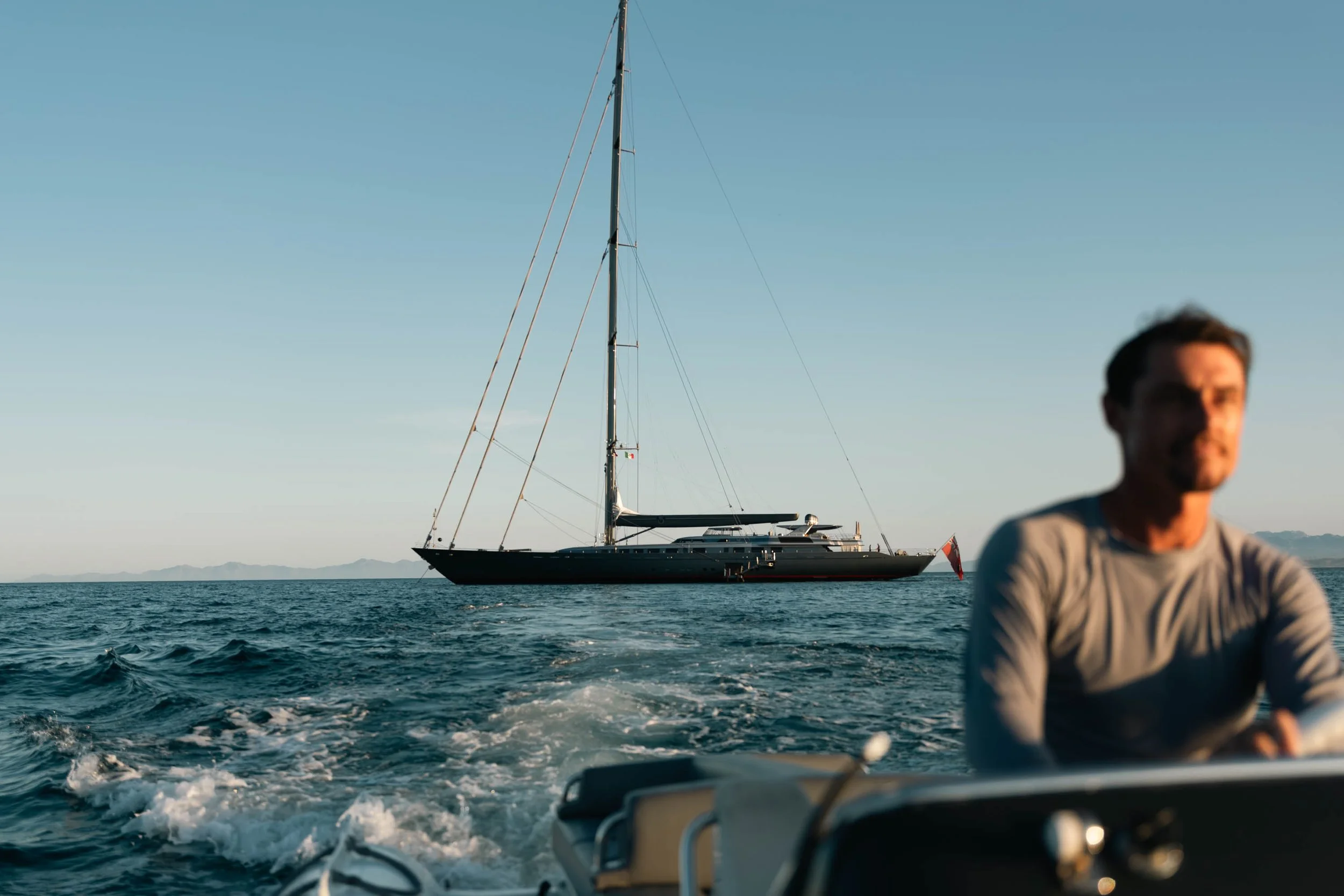 Man on speedboat with large sailboat in background on ocean.