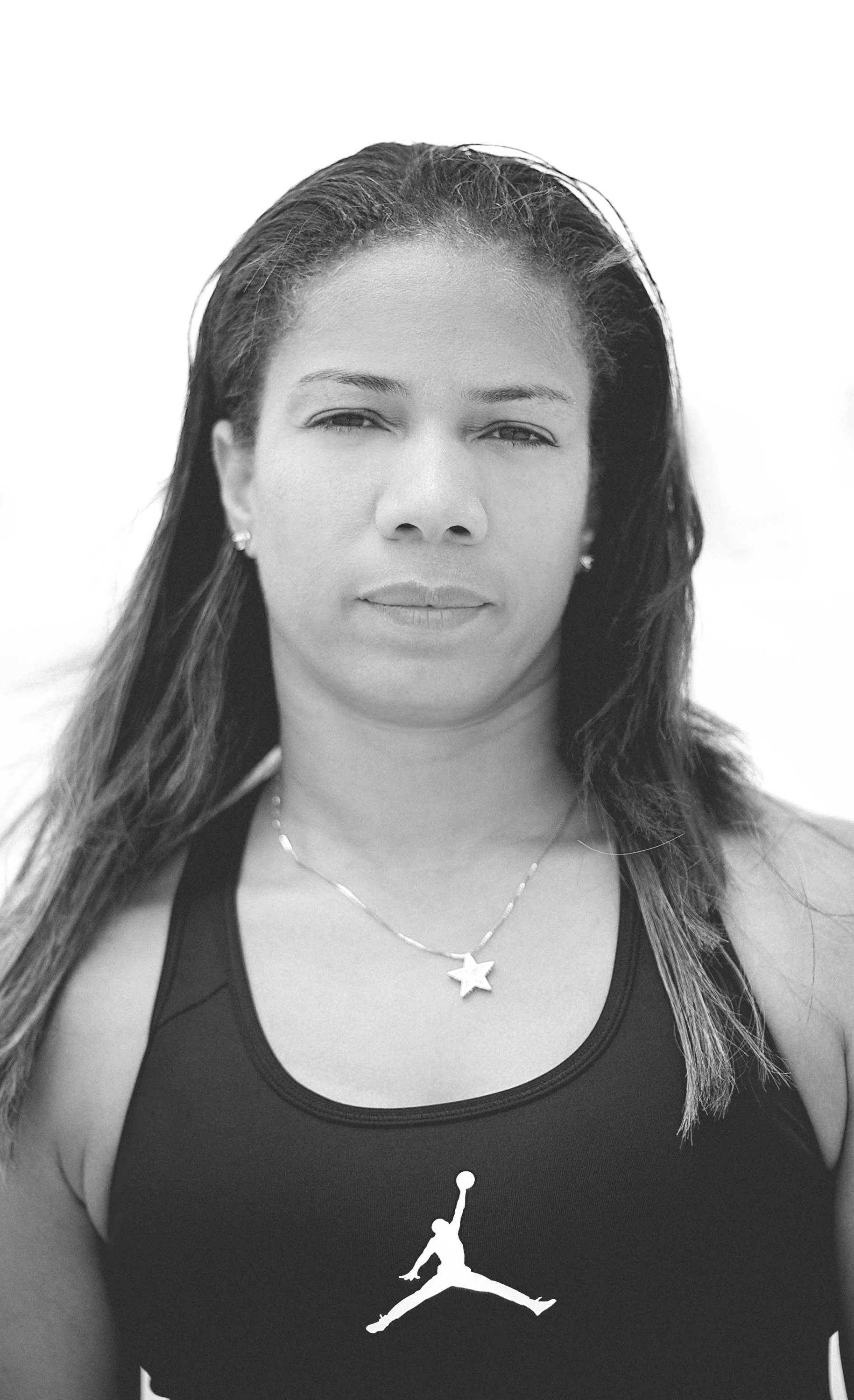 Black and white portrait of a woman with long hair, wearing a black top featuring the Air Jordan logo, and a necklace with a star pendant.
