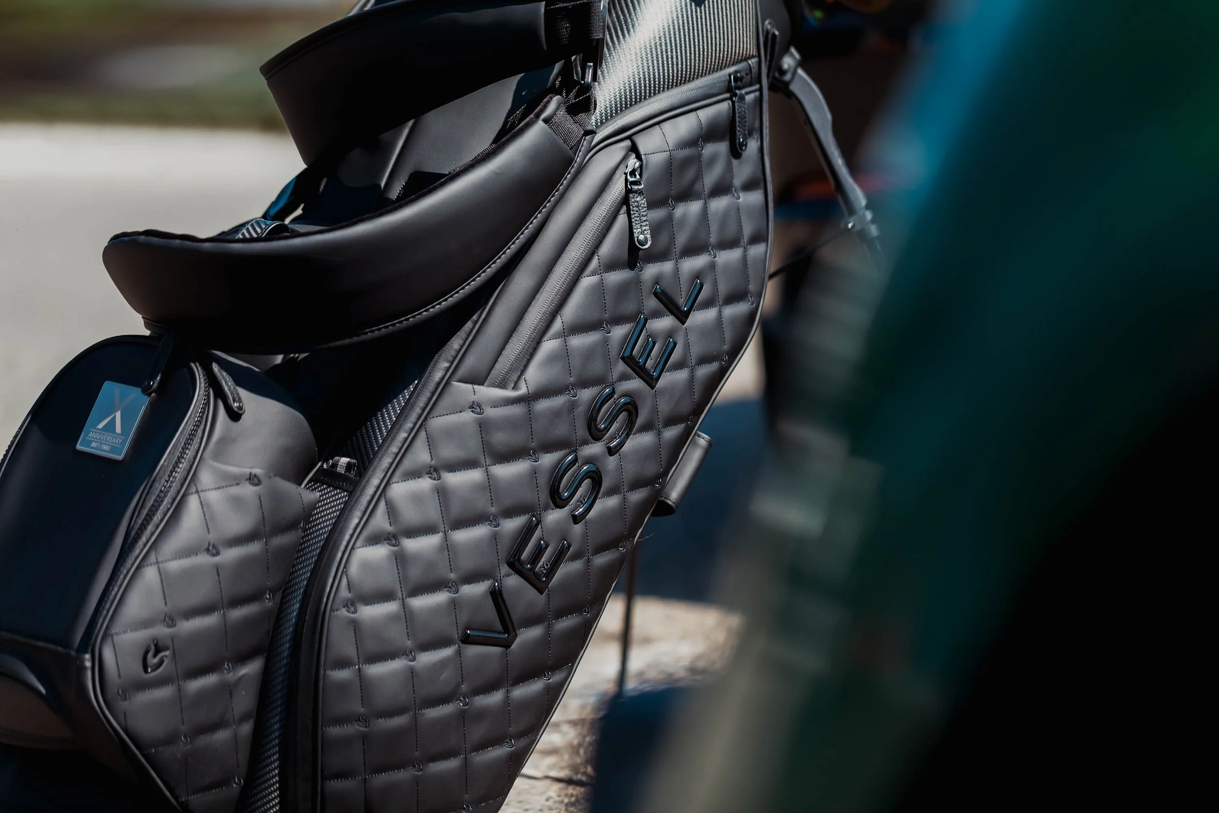 Close-up of a black quilted golf bag with the logo "VESSEL" embossed on the side.
