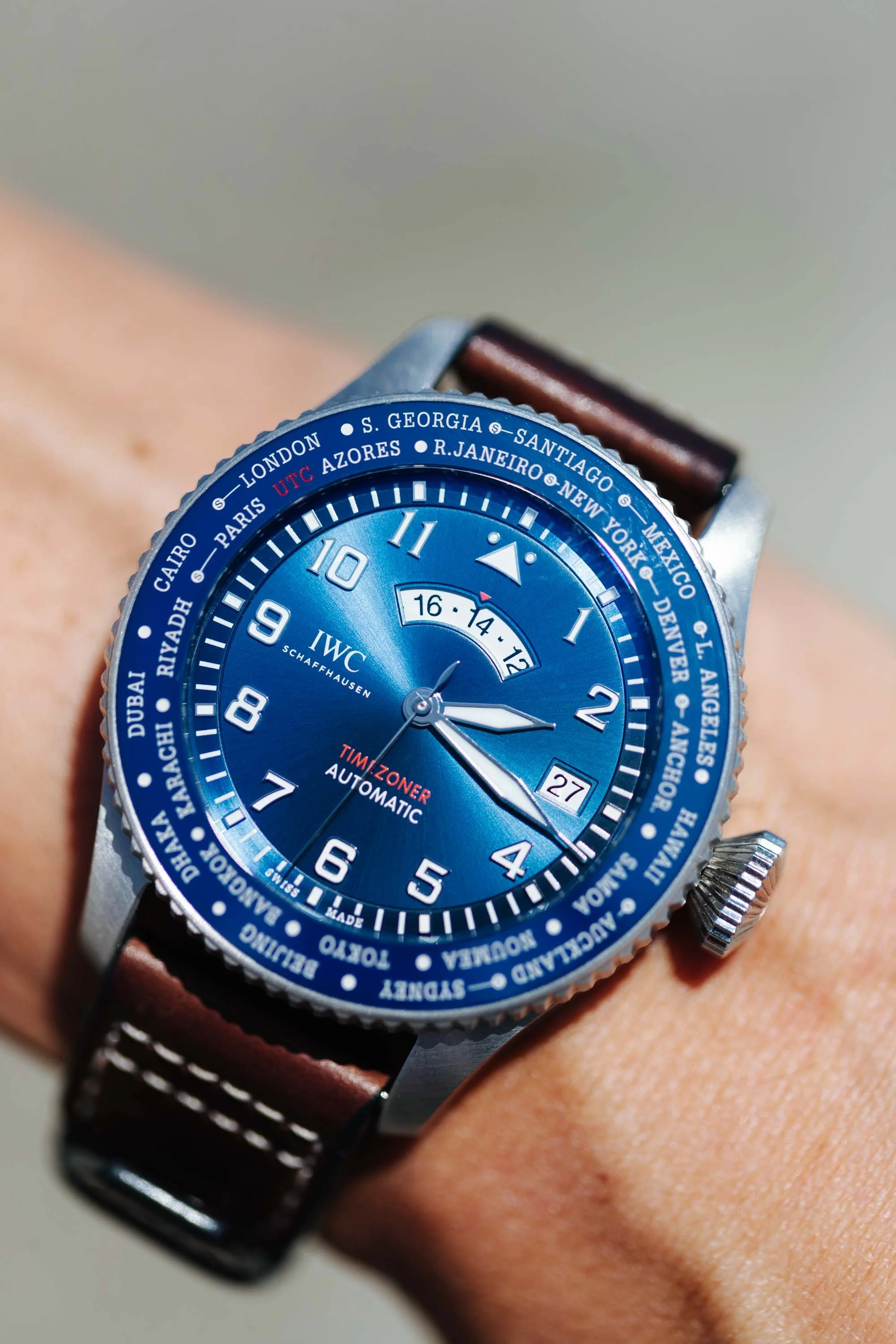 Close-up of a blue dial wristwatch with world time zones, leather strap, and IWC Schaffhausen branding.