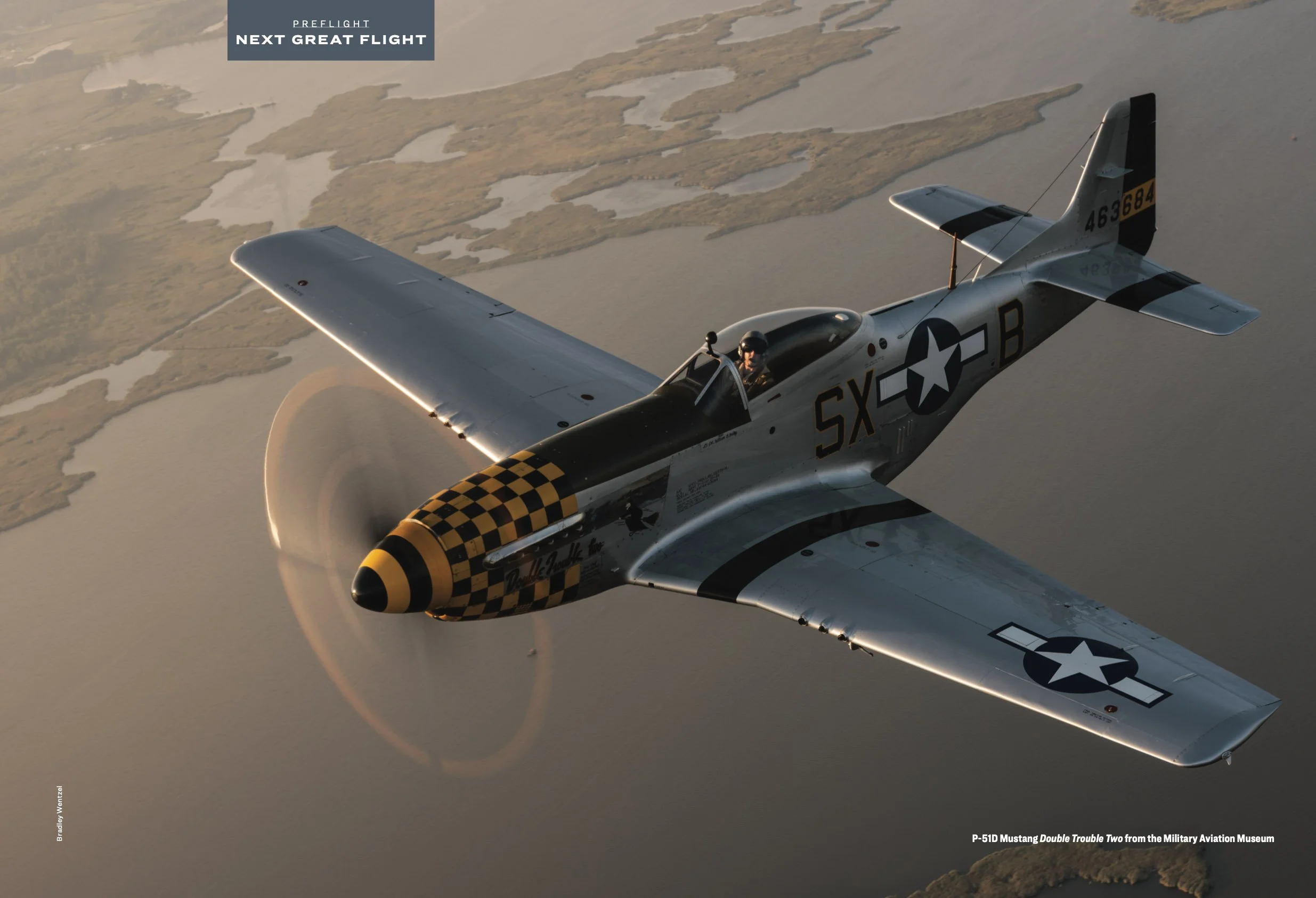 Vintage P-51D Mustang aircraft in flight over a landscape, featuring a checkered nose design and military markings.