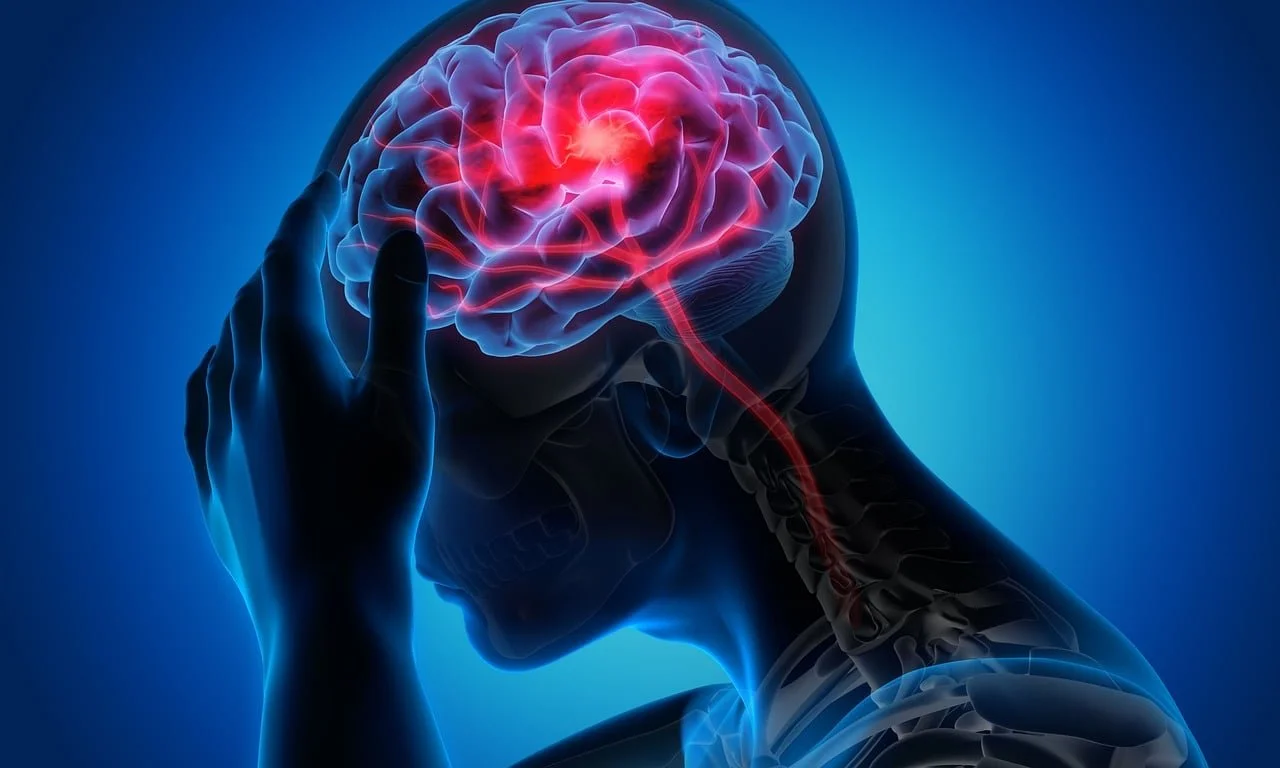 An image of a silhouette of a persons head and neck with their hand on their head. The brain can be seen and is highlighted red to represent a migraine.