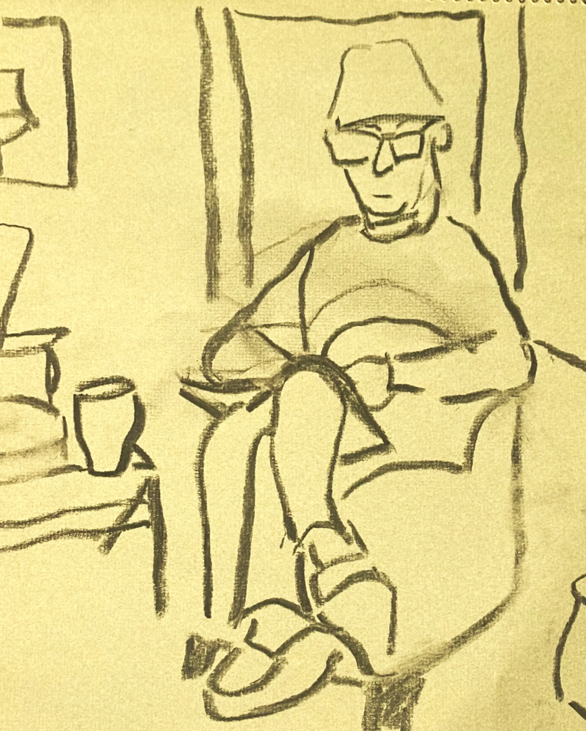 Charcoal sketch of a seated figure with legs crossed, a mug resting on a small table beside him.
