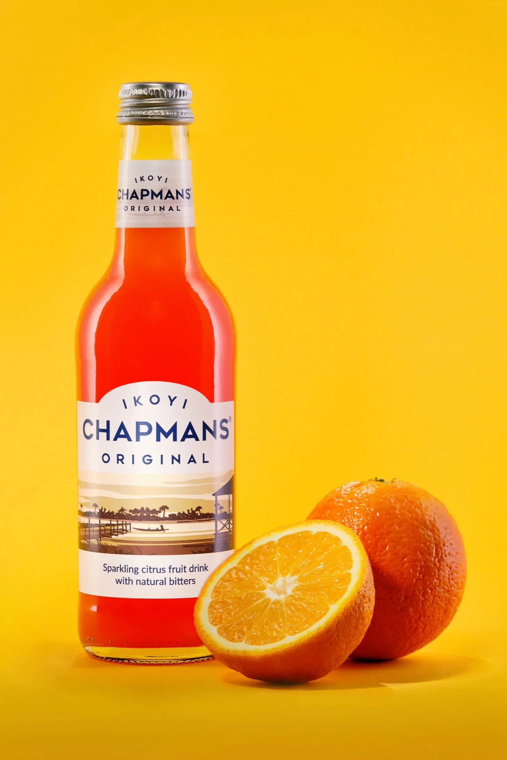 Product photography - a bottled soft drink with sliced orange fruit on vibrant yellow background