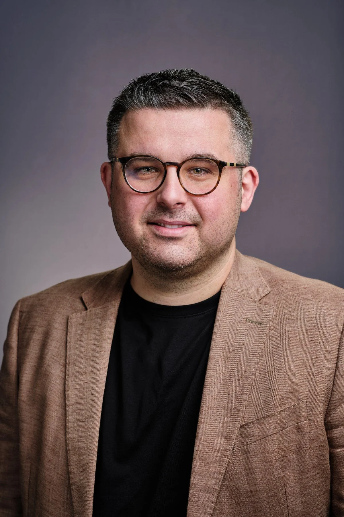 Professional headshot photo of a man in a tan jacket