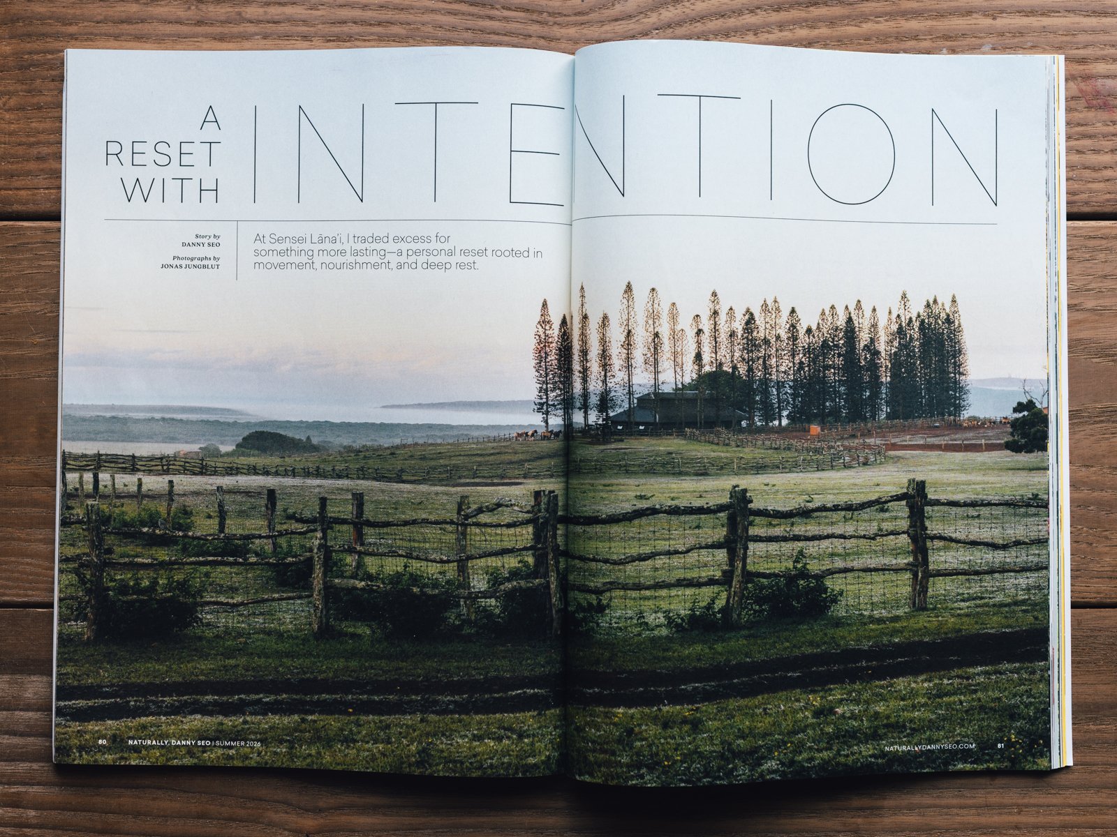 Open magazine displaying a scenic landscape of a grassy field with wooden fences, trees, and hills in the background.