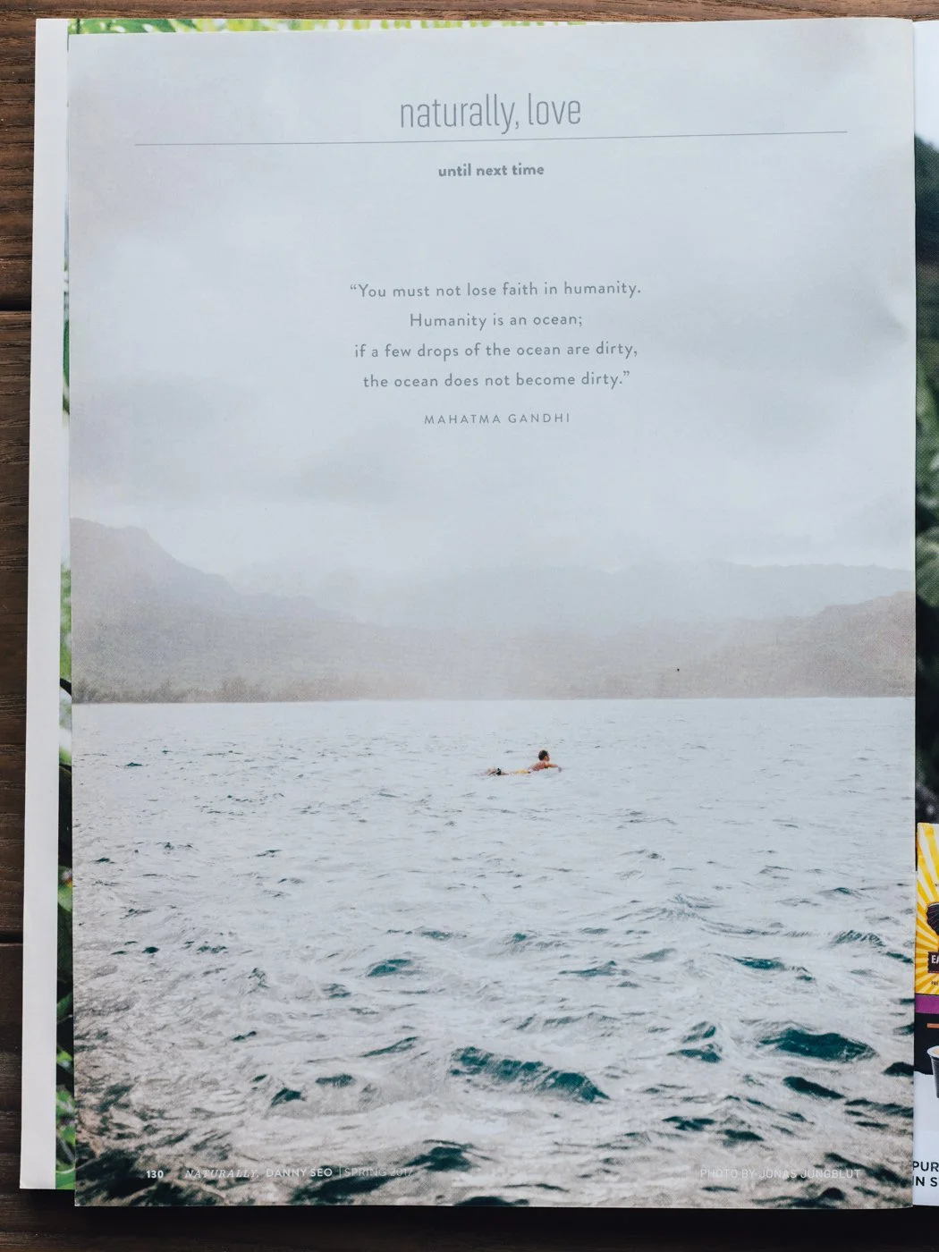 A person swimming in a large, calm body of water with mountains in the background, overlaid with a quote about humanity and the ocean.