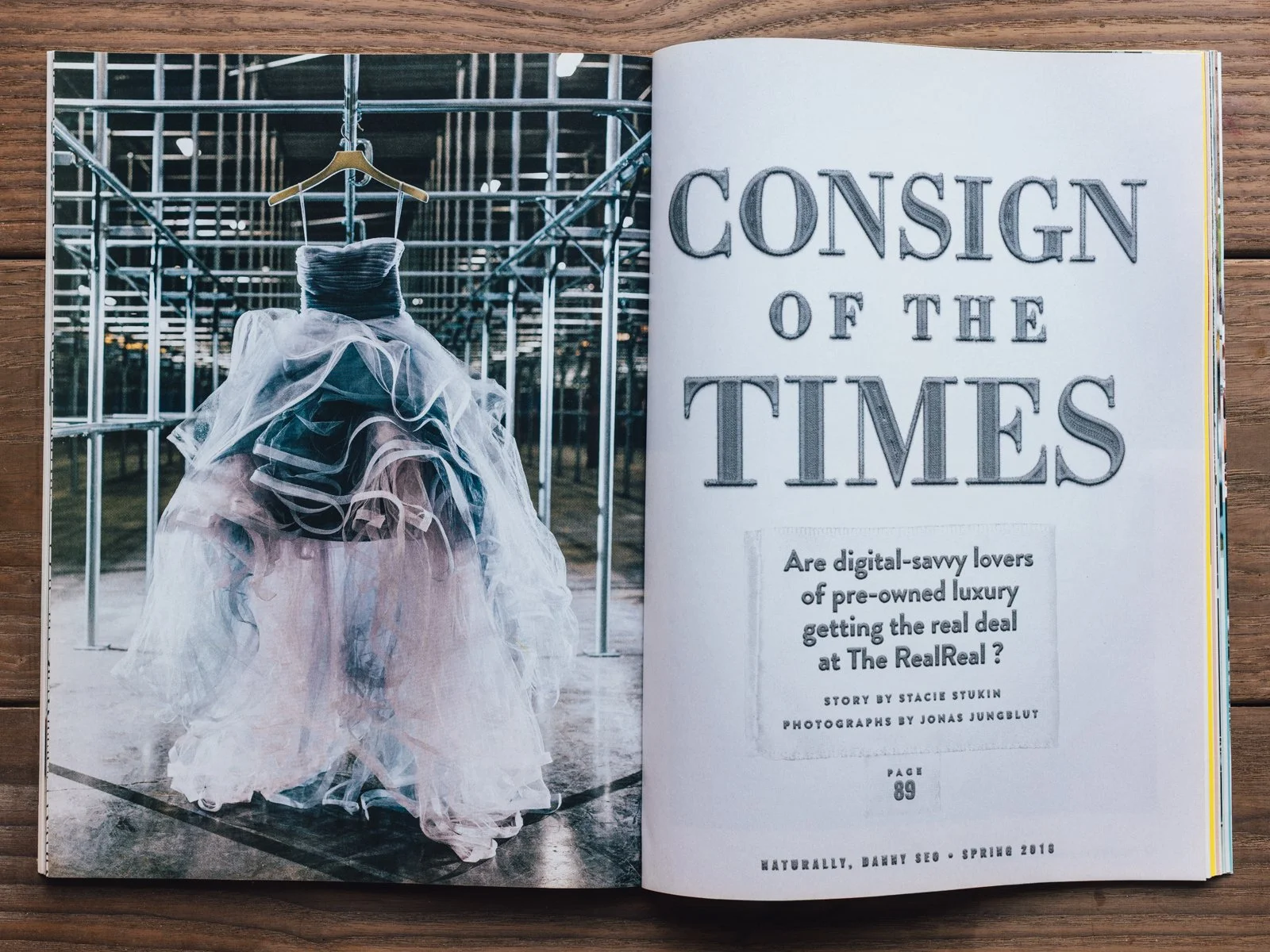 Photo of a dress made of various fabrics hanging on a hanger in an outdoor setting with metal scaffolding and trees in the background.