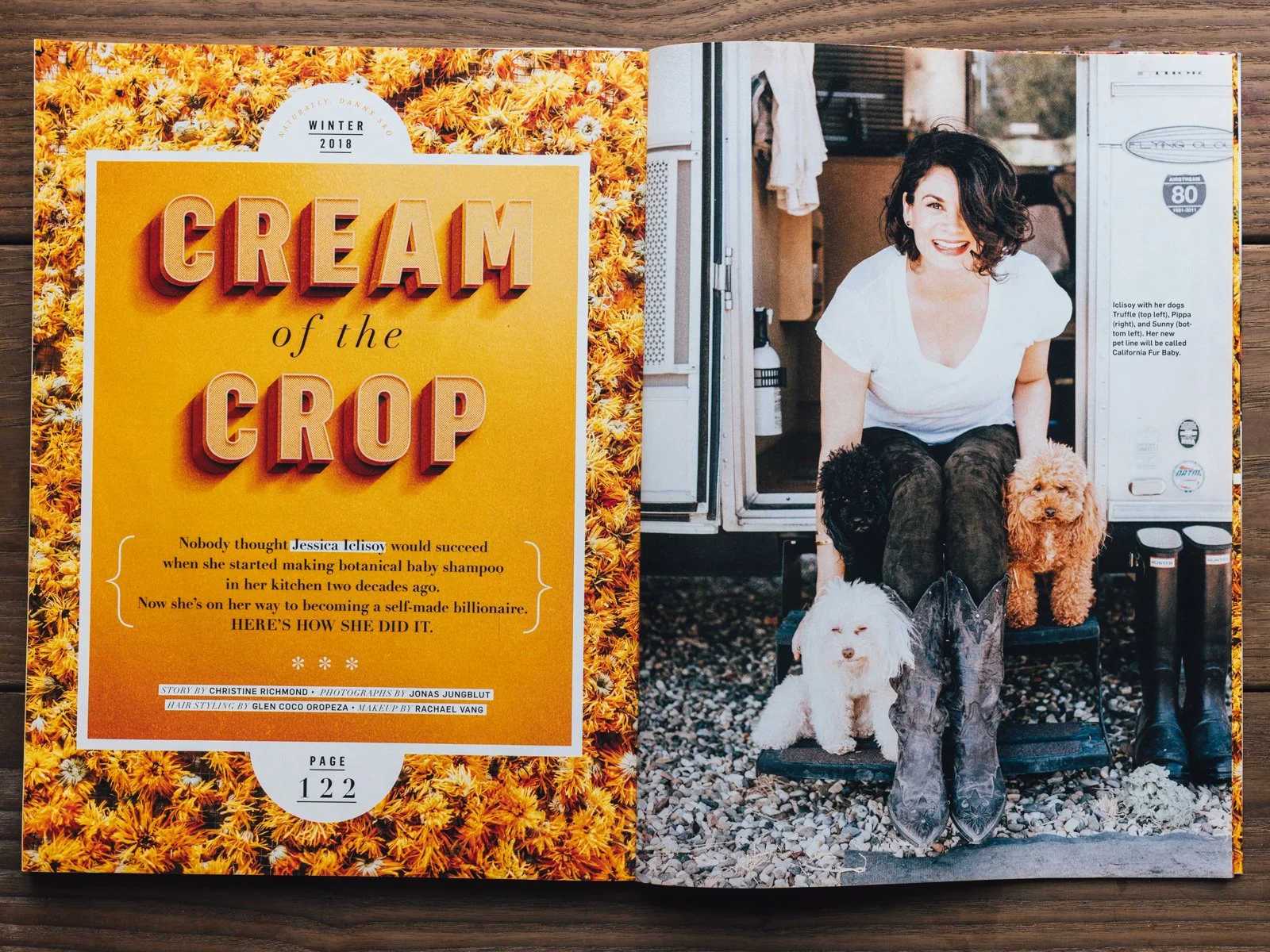 A magazine spread with a bold yellow and orange cover on the left titled "Cream of the Crop" and a photo of a woman with curly dark hair smiling, sitting outside her food truck with three small poodles around her on the right.