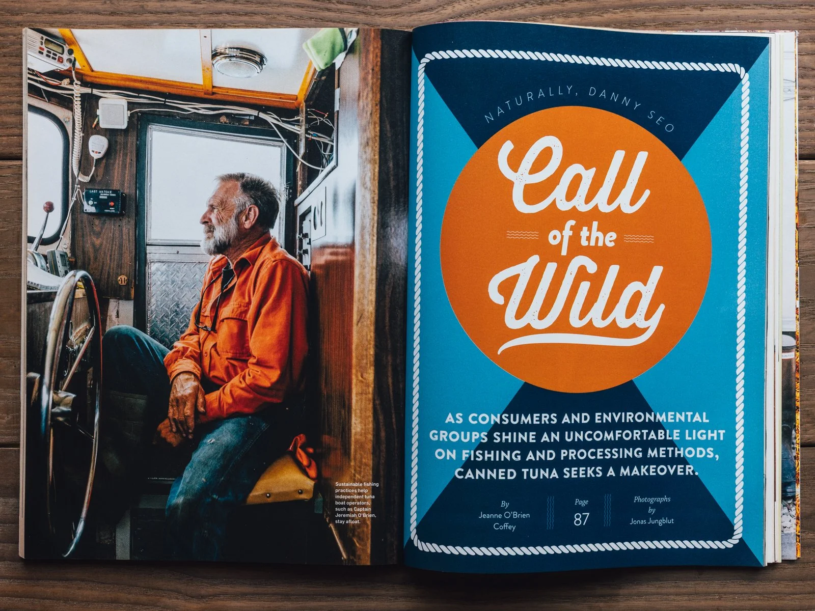 A man with gray hair and beard, wearing an orange shirt, sitting inside a fishing boat with various controls and wires visible around him. The boat has a window behind him and the photo is titled "Call of the Wild" on the adjacent magazine page.