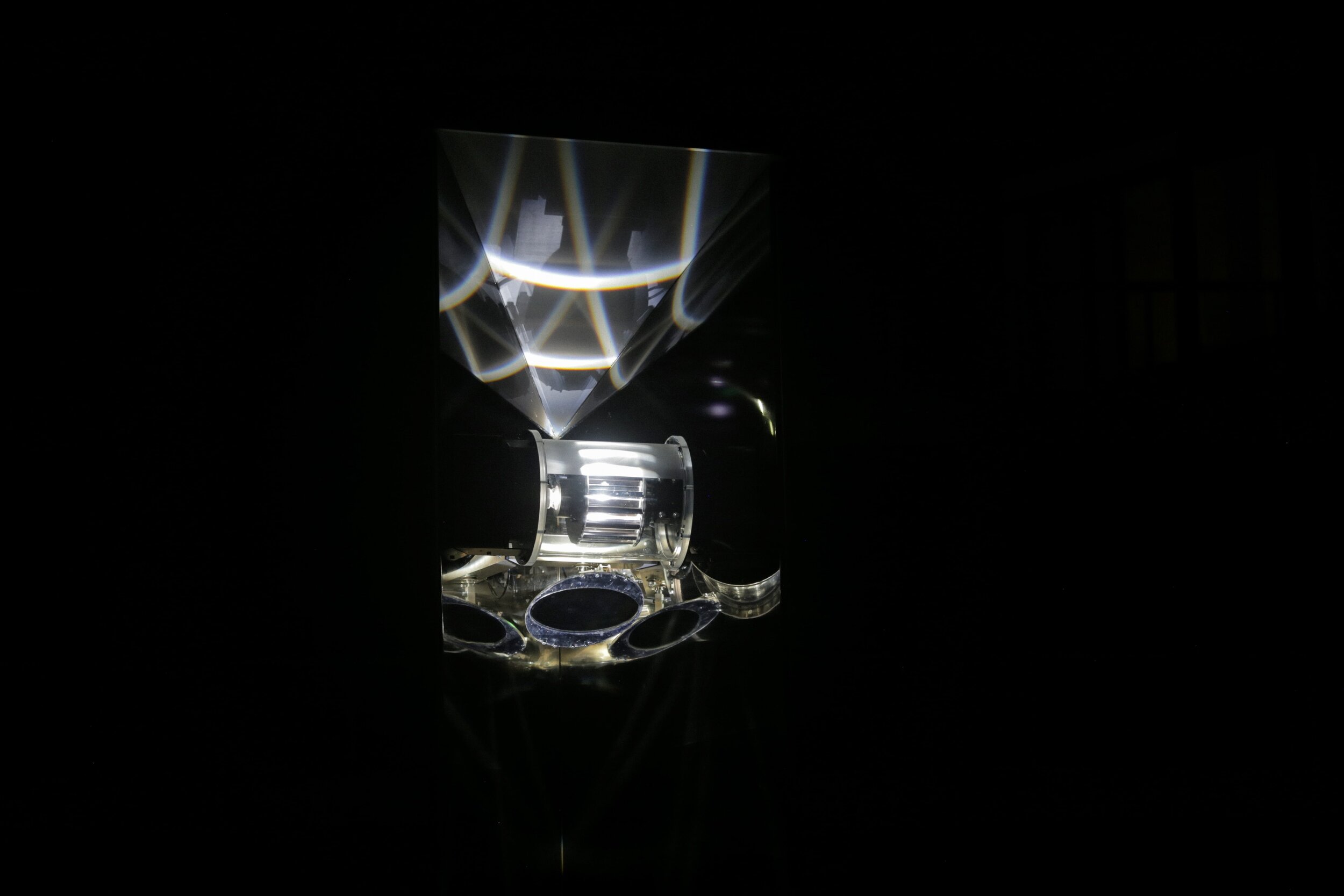 Close-up of a diamond-shaped optical instrument with reflections and metallic components, in a dark background.