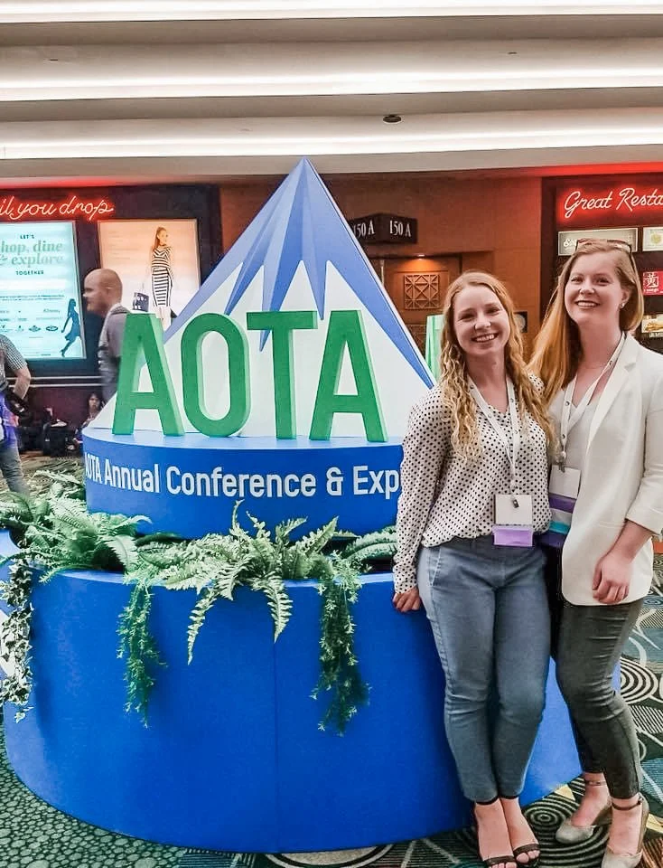 Two women standing in front of AOTA Annual Conference sign