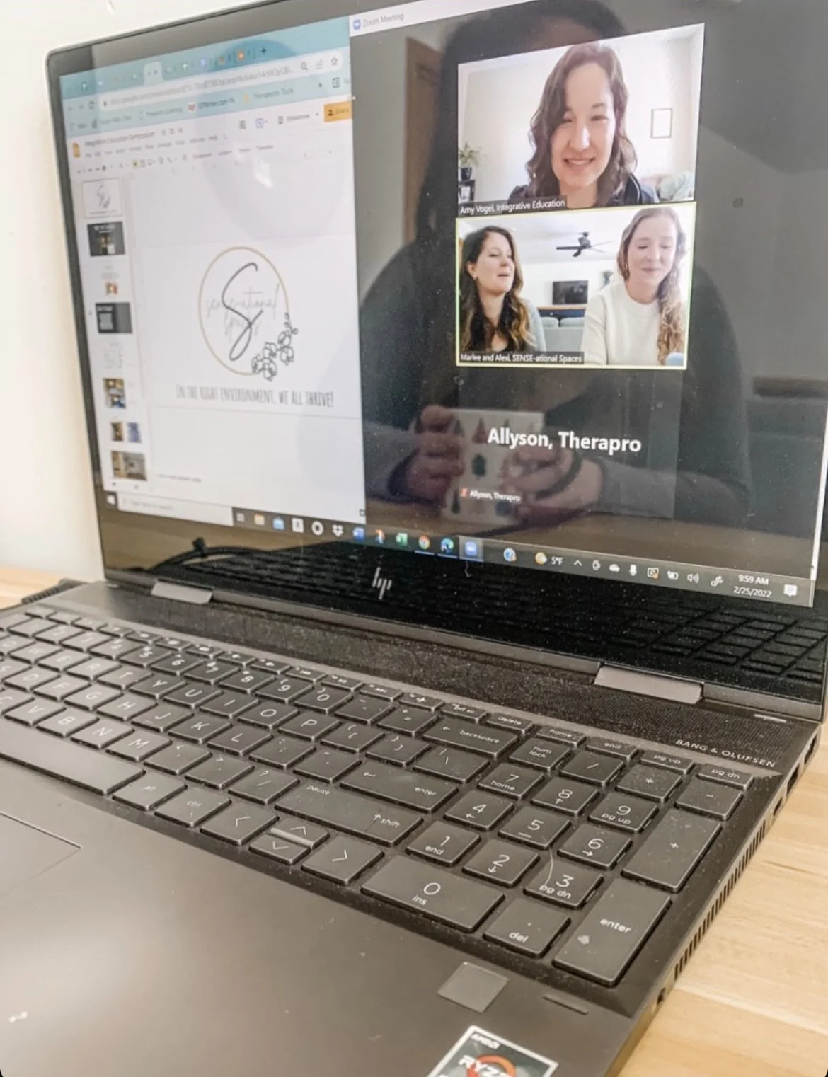 Laptop screen showing a video call with three participants, a slide deck on the left, and a keyboard below.