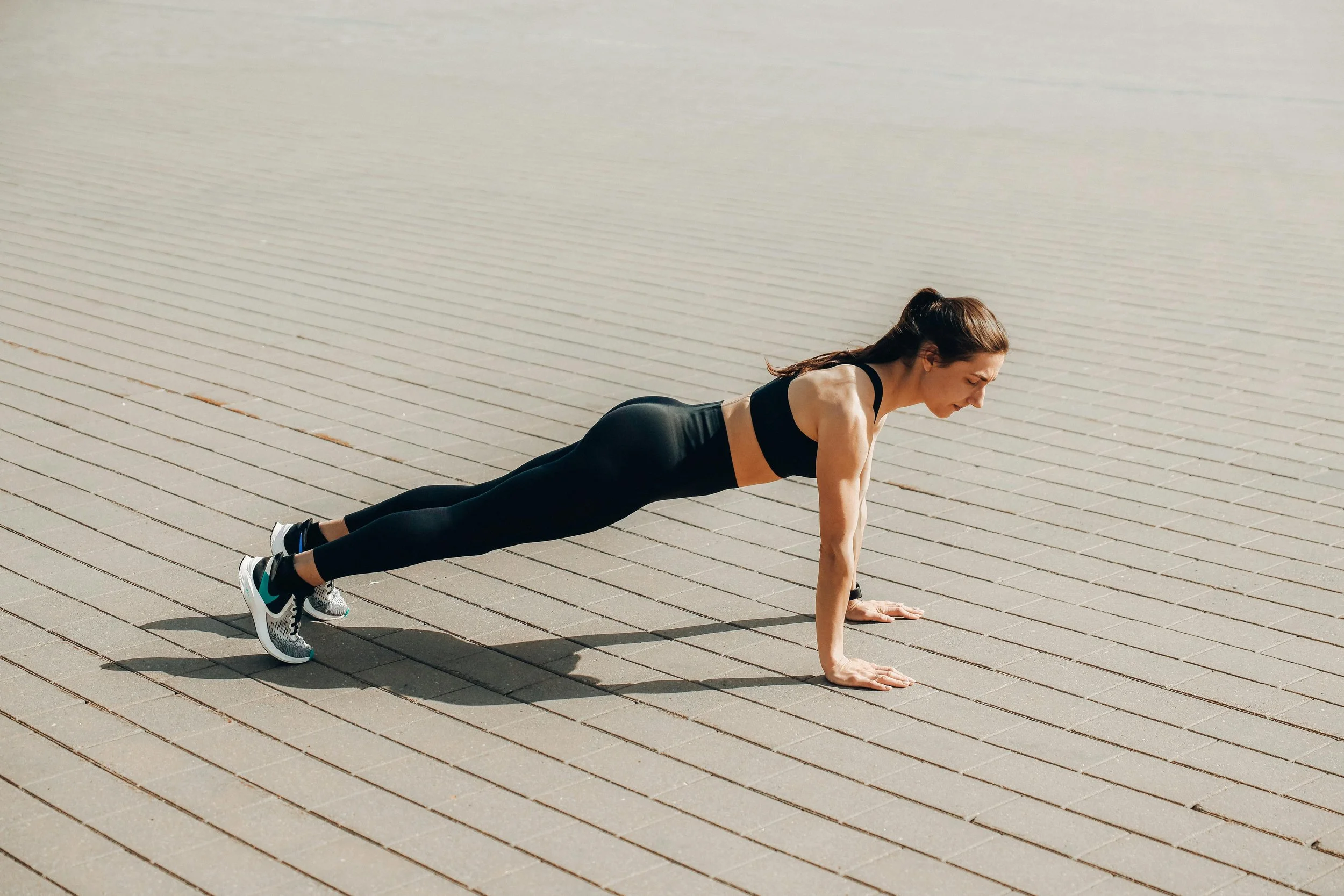 A person in fitness attire performs a push-up on a textured gray outdoor surface, showcasing strength and focus.