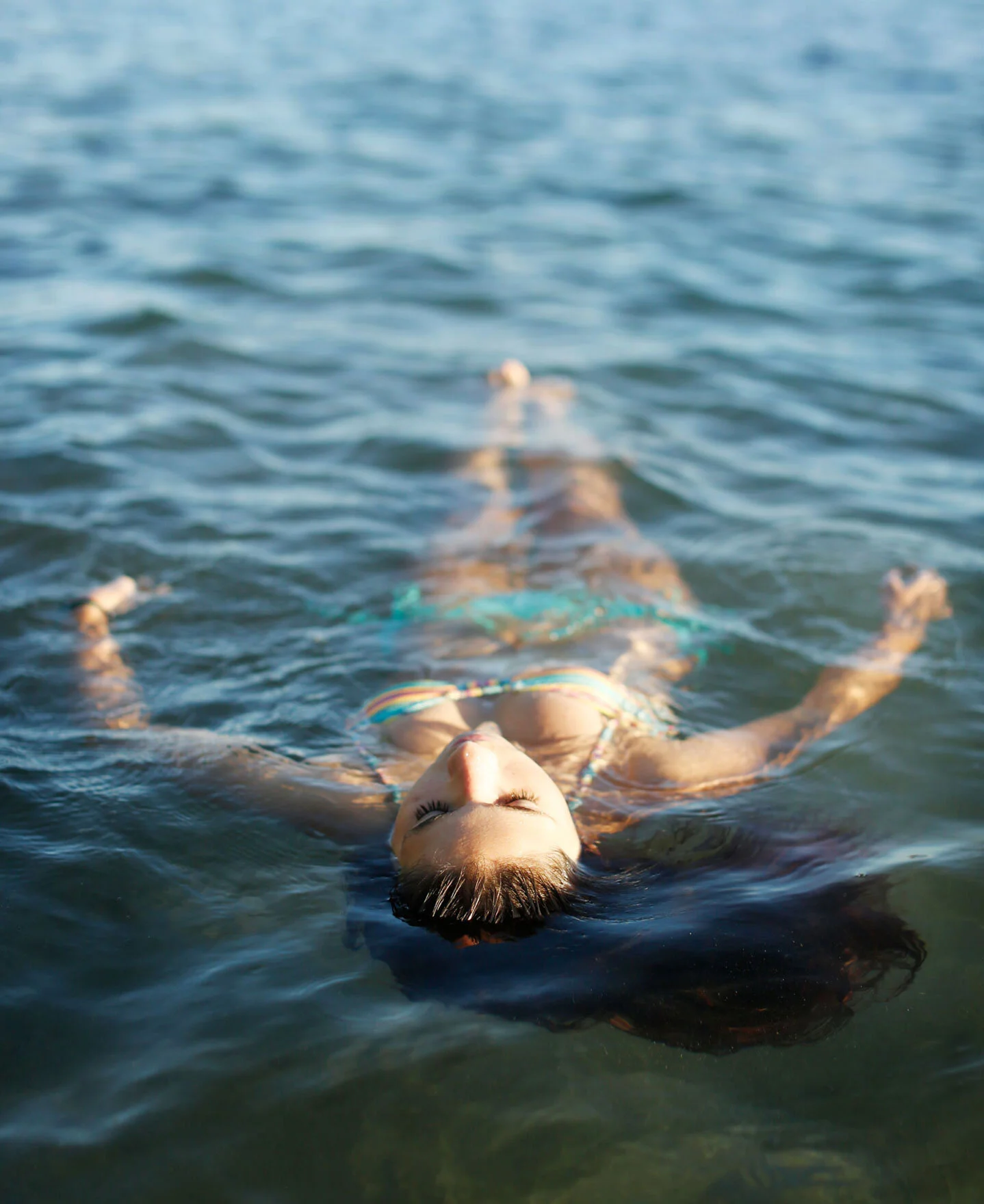 A teenager with dark hair floating on her back in a body of water with her eyes closed in a meditative state in Maui, Hawai'i.