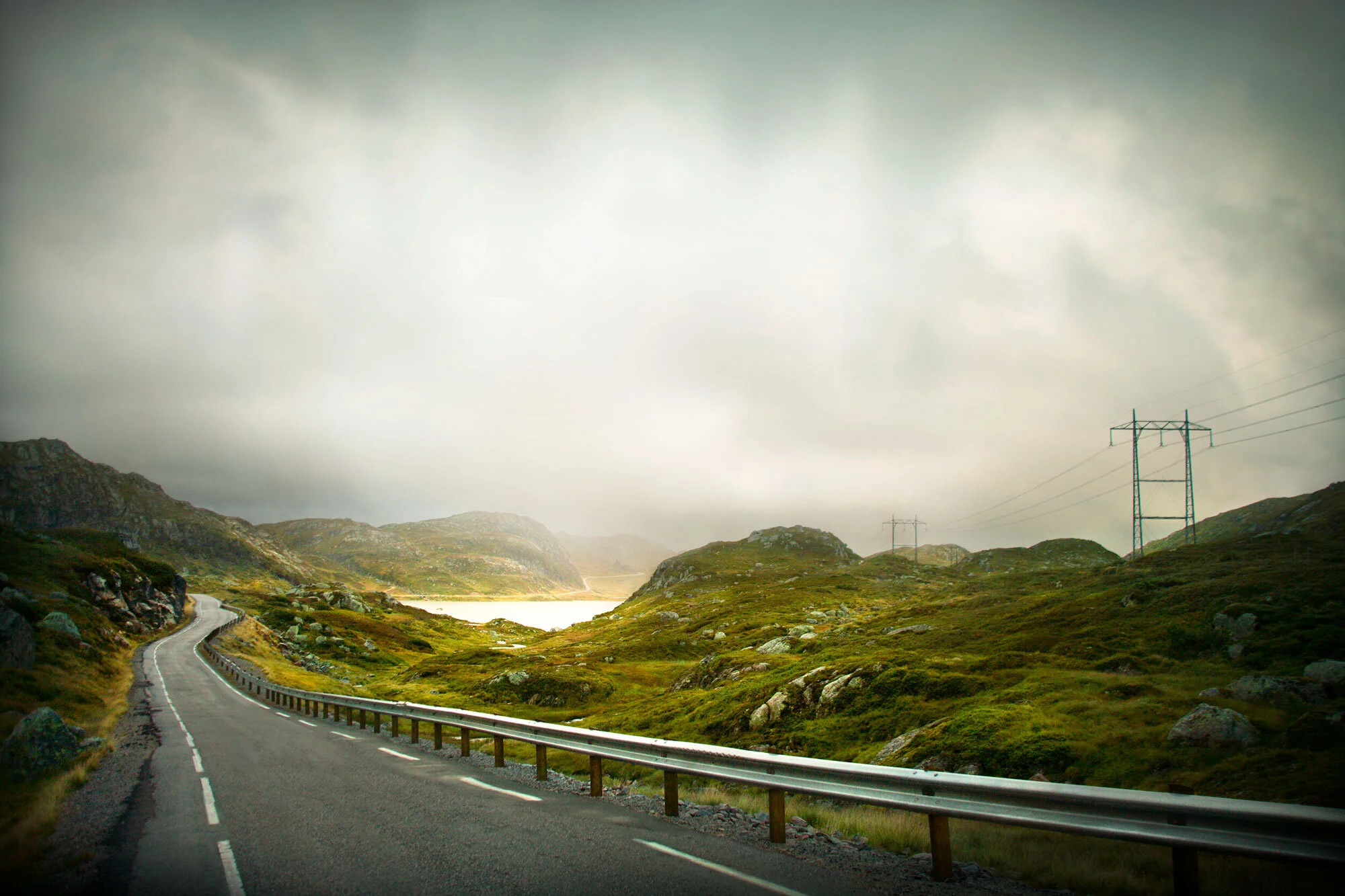 Windy rand narrow oad in Norway leading to the Pulpit Chair  in Norway on a cloudy and rainy afternoon against green hills and a guard rail.