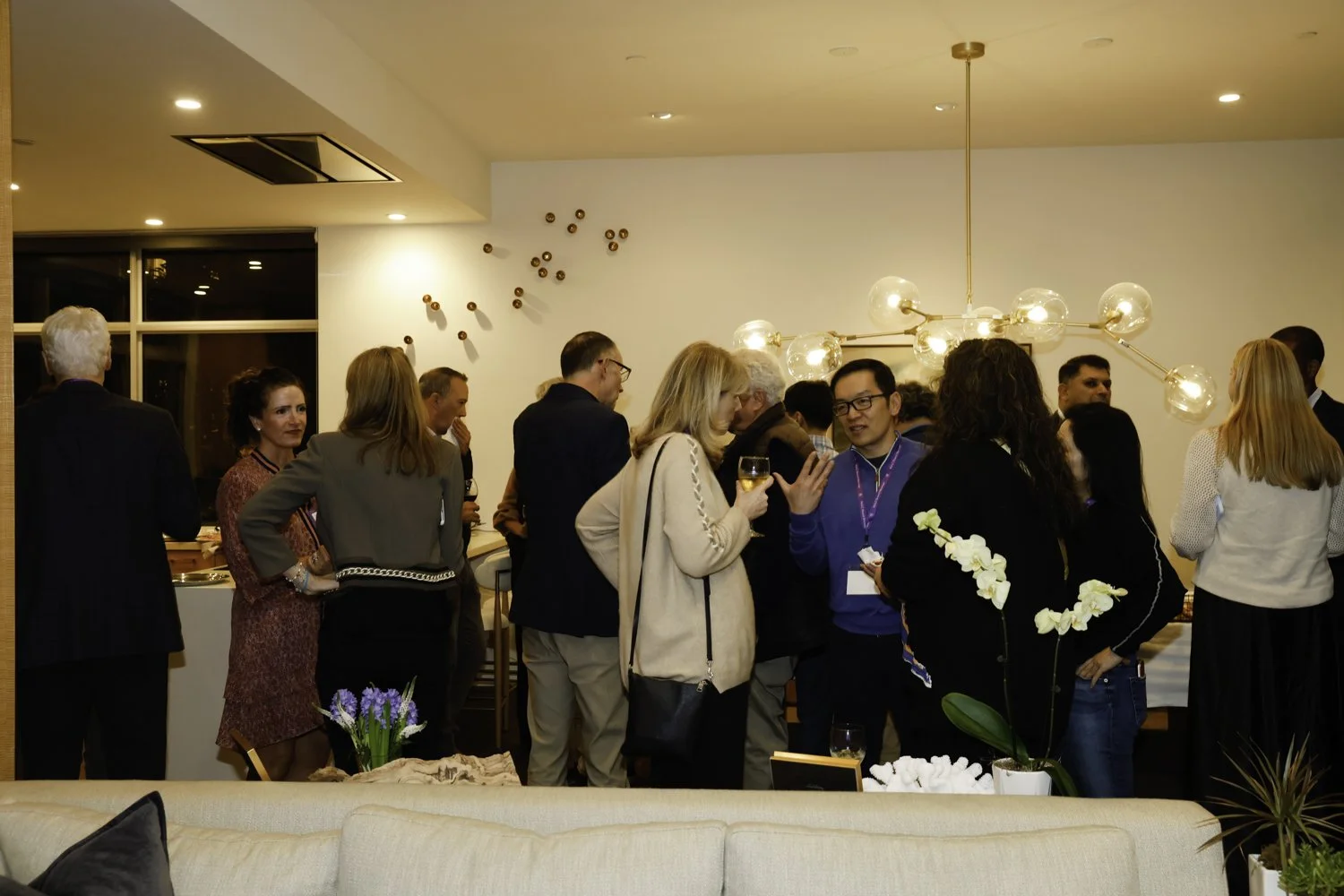 A group of people socializing at a candlelit dinner party in an upscale room with modern decor, including a large chandelier and wall art Brex headquarter in San Francisco, CA.