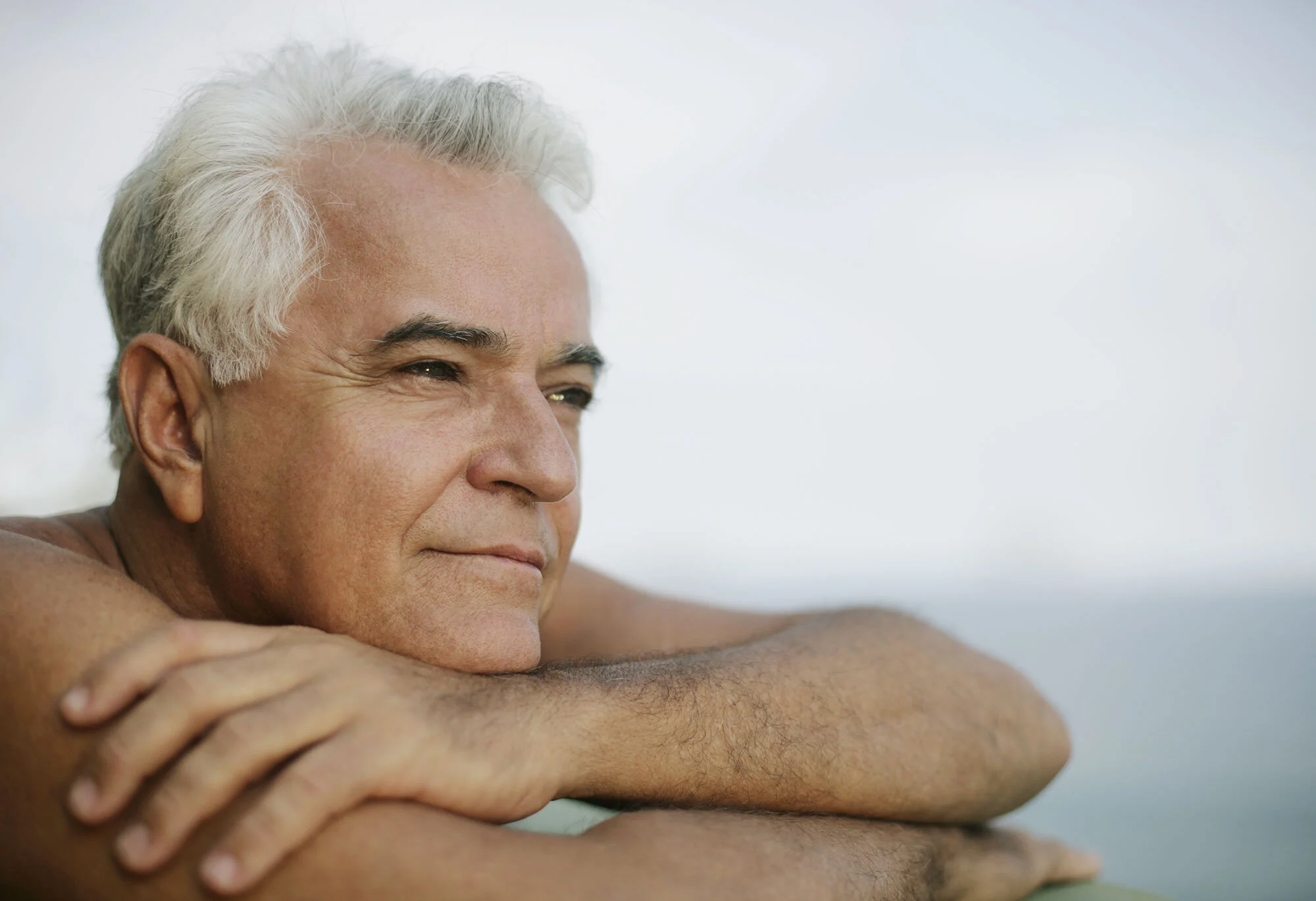 Close-up of a middle-aged white Brazilian man with gray hair and white skin relaxing outdoors, resting his arms on a surface, with a calm and contemplative expression, on a blurred light background at Ipanema beach in Rio de Janeiro, Brazil.