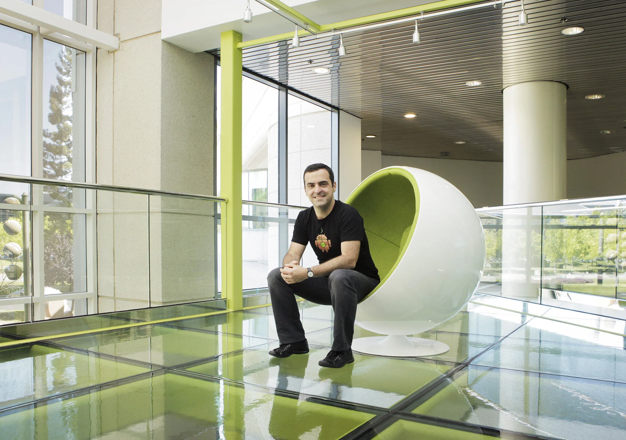 Brazilian Hugo Barra sitting in a modern, egg-shaped chair inside a building with large windows and green accents at Google head quarter in Mountain View, CA.