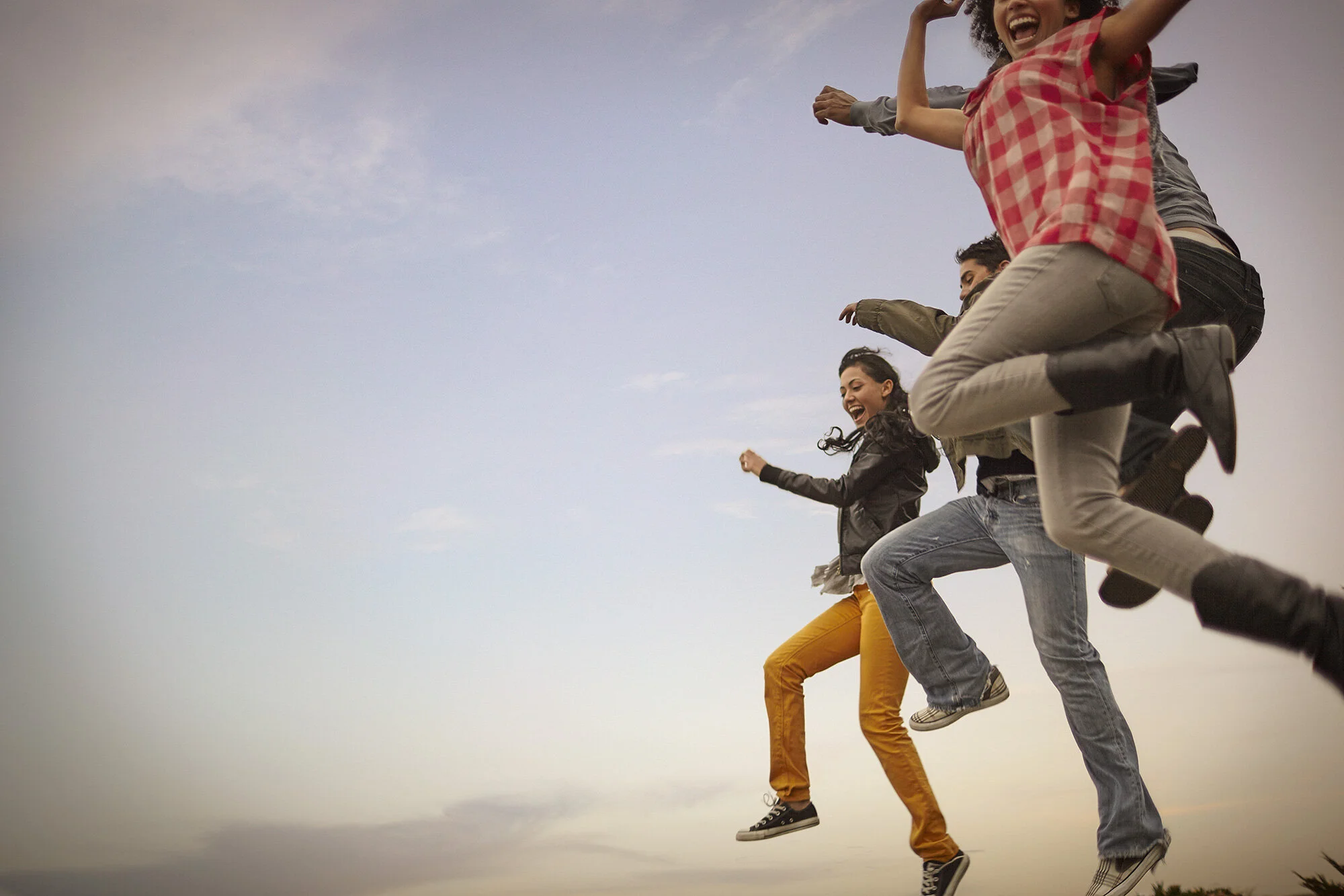 Four young adults joyfully jumping in the air outdoors during sunset, smiling and expressing happiness and joy in San Francisco, CA.