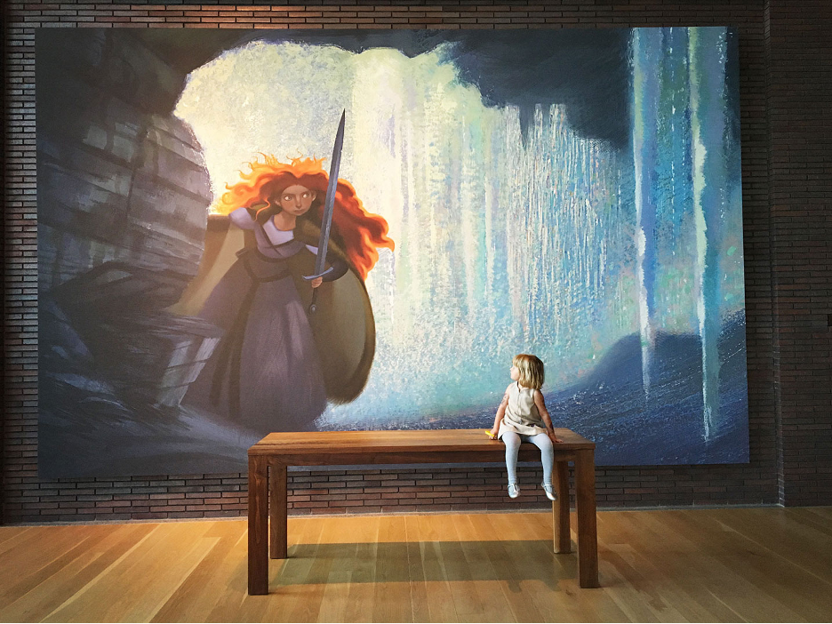 Young girl sitting on a table looking back at a big painting of Merida from the Pixar movie, at Pixar, Emeryville, CA.