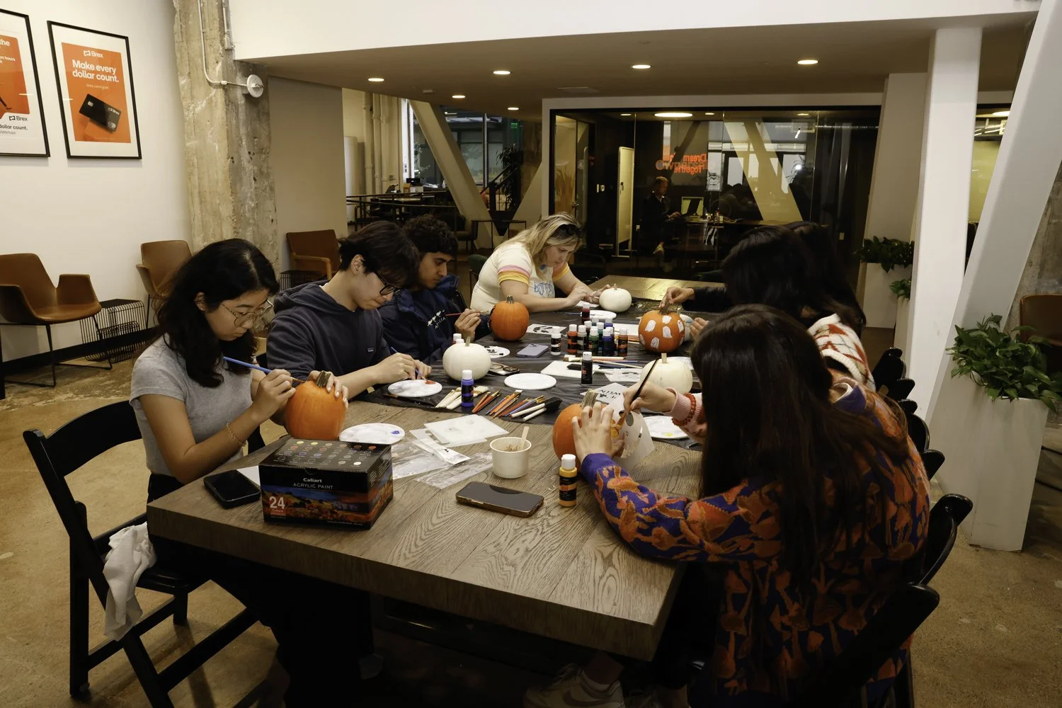 Group of six people painting pumpkins at a craft workshop in a cozy, modern room Brex headquarter in San Francisco, CA.