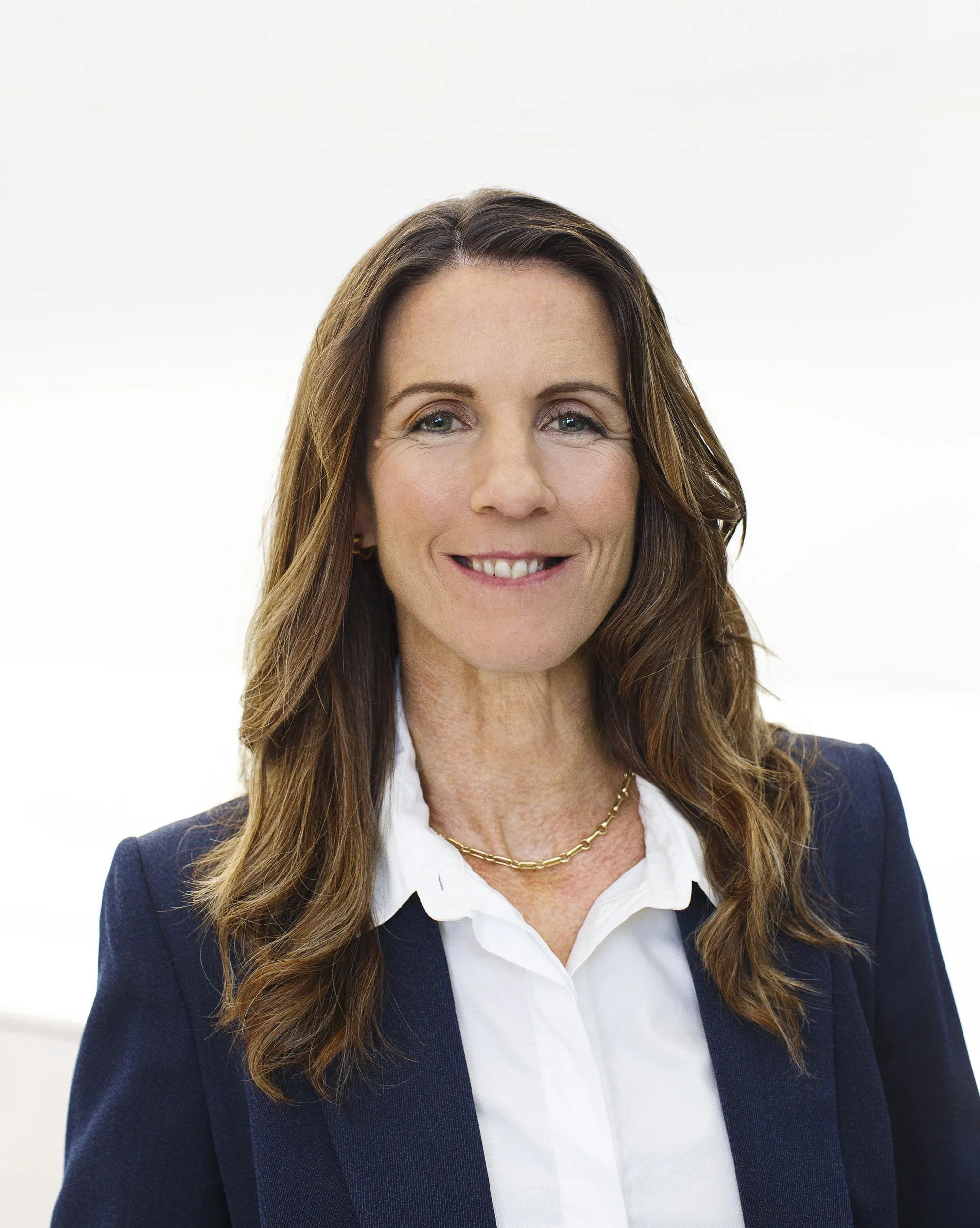 White woman CMO wearing a white shirt and blue blazer, shoulder length hair and a necklace, standing at Hewlett Packard's office in Palo Alto, CA.